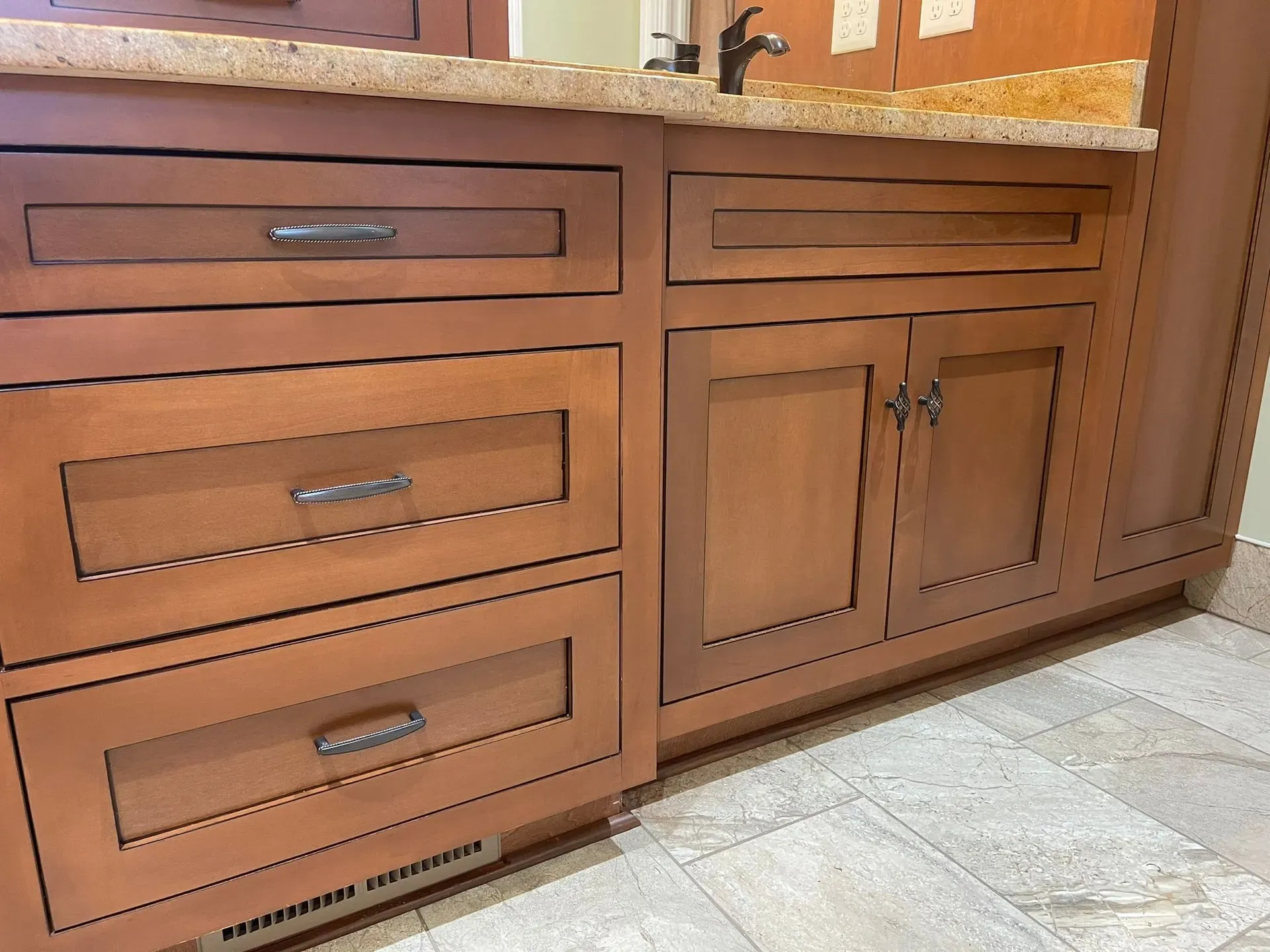 Brown kitchen cabinets with drawers and double doors under a granite countertop, beside a tiled floor