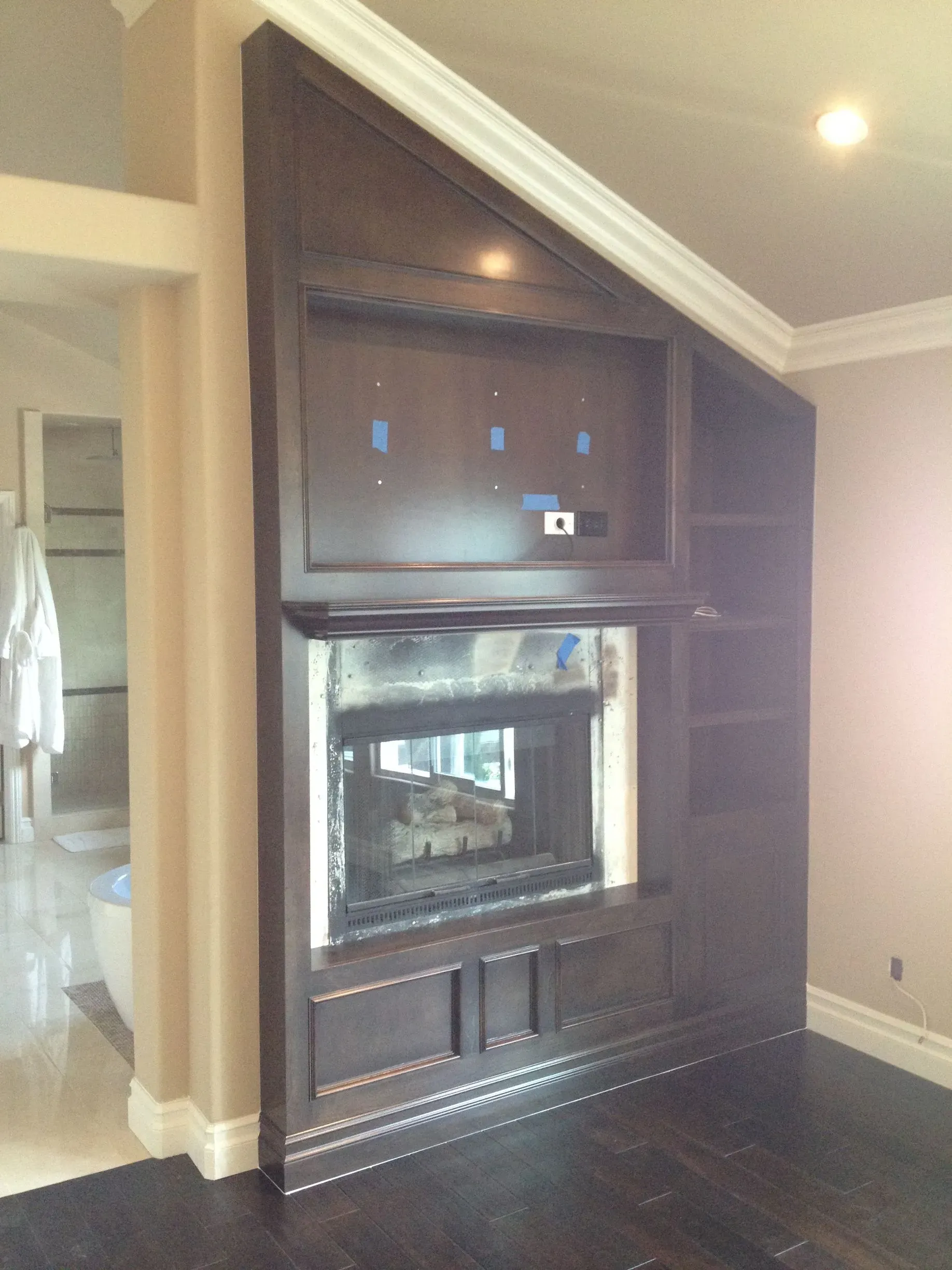 Built-in dark wood fireplace surround with TV above and recessed shelving in a beige room