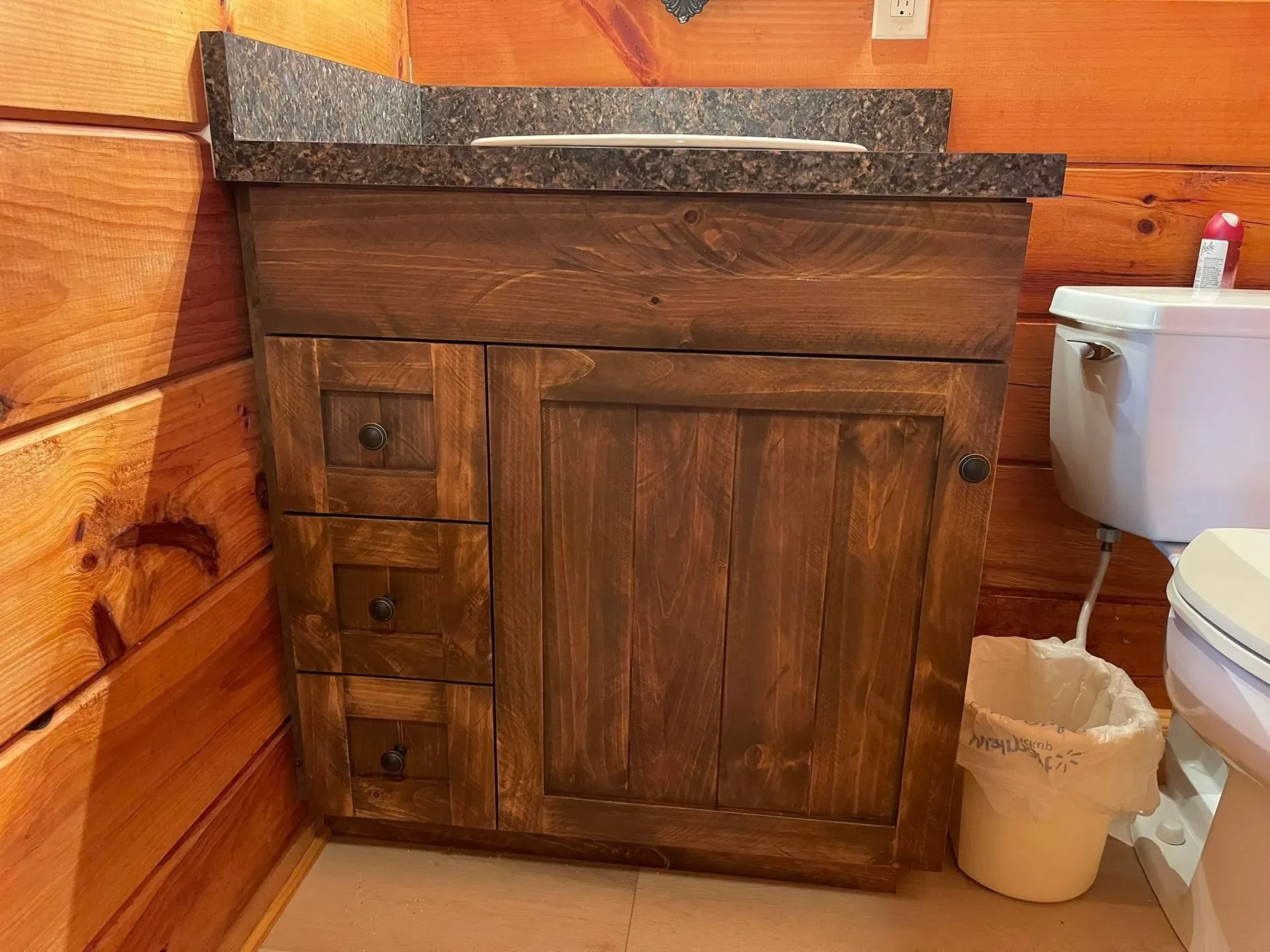 Rustic wooden bathroom vanity with dark countertop and toilet beside it