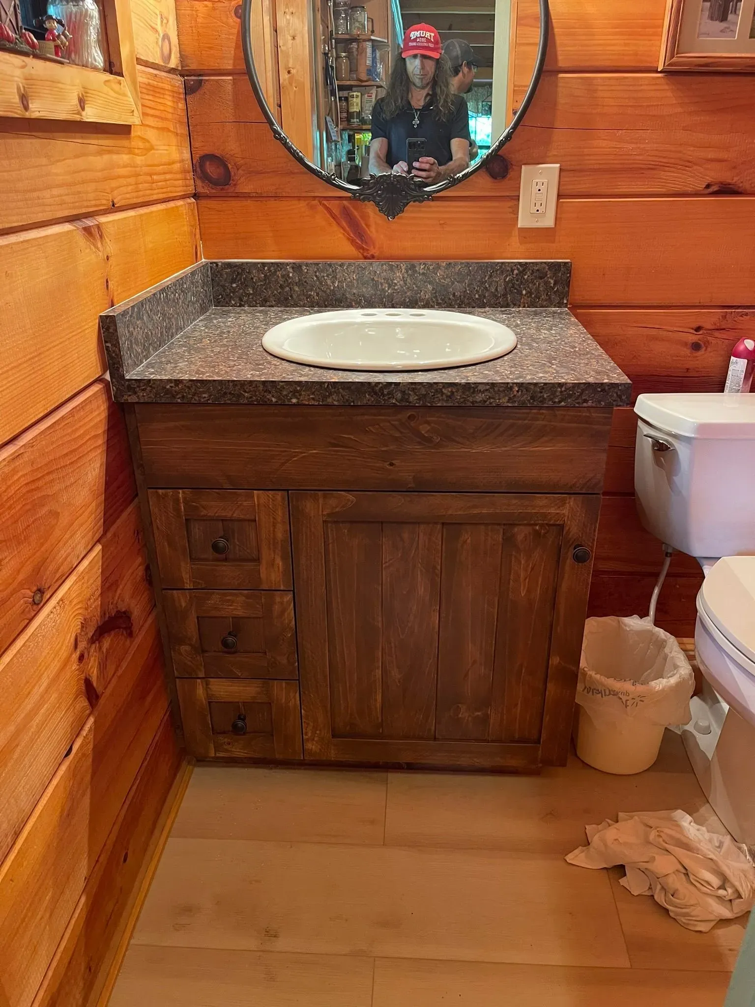 Rustic bathroom vanity with white sink, granite countertop, wood cabinet, mirror, and toilet.