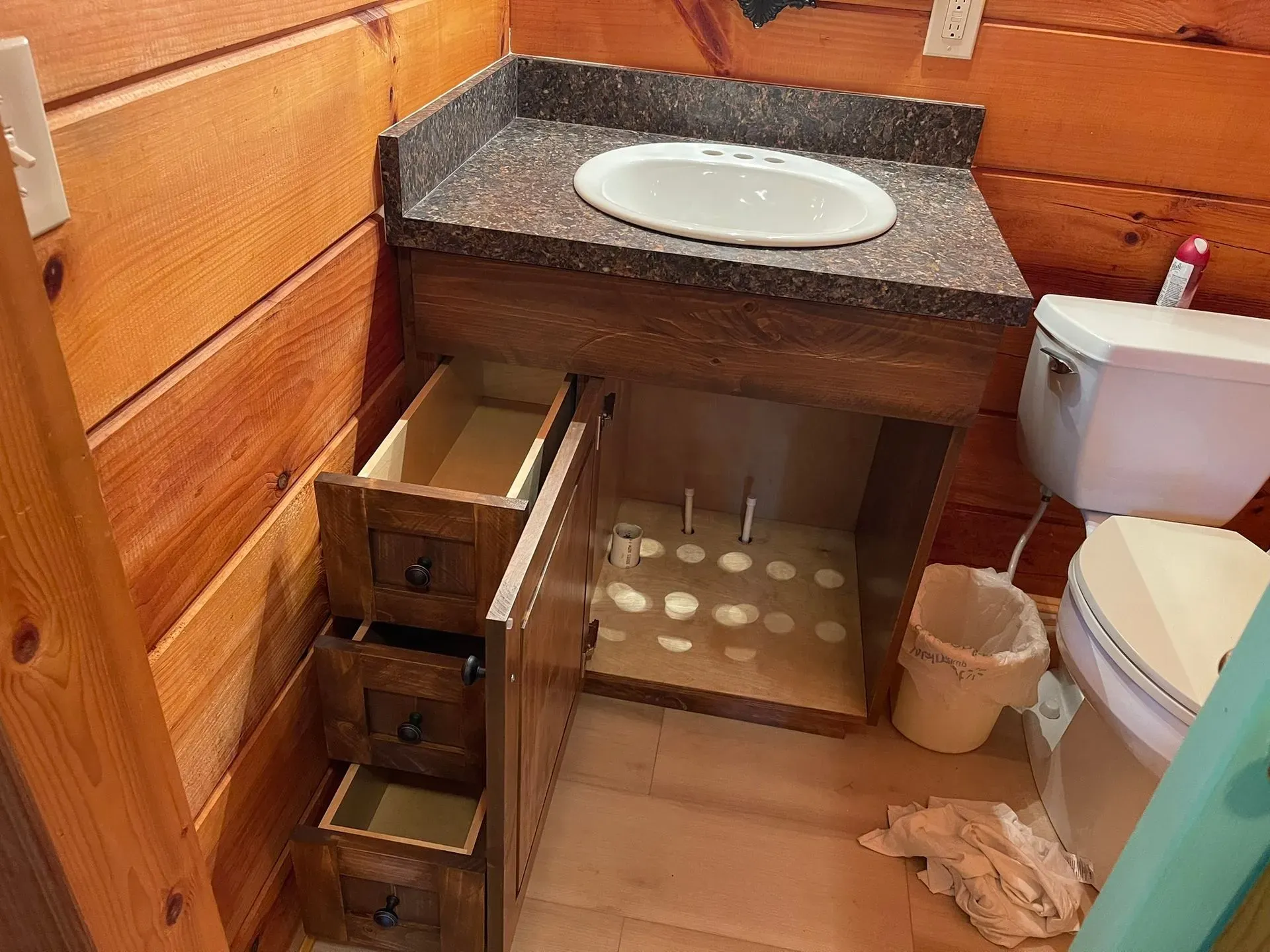 Rustic bathroom with wooden walls, stone sink counter, open drawers, and a toilet beside it