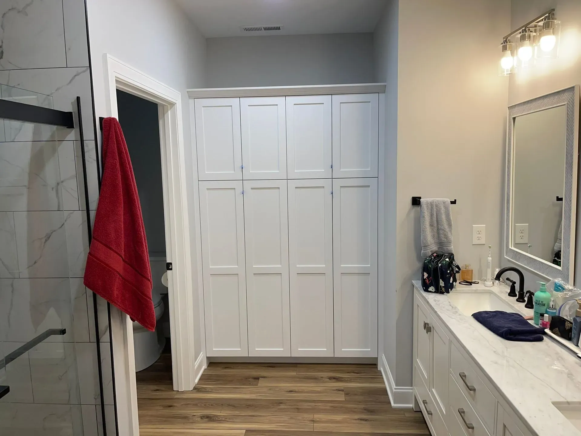 Bathroom with double vanity, large mirror, white cabinets, red towel, and walk-in closet doors.