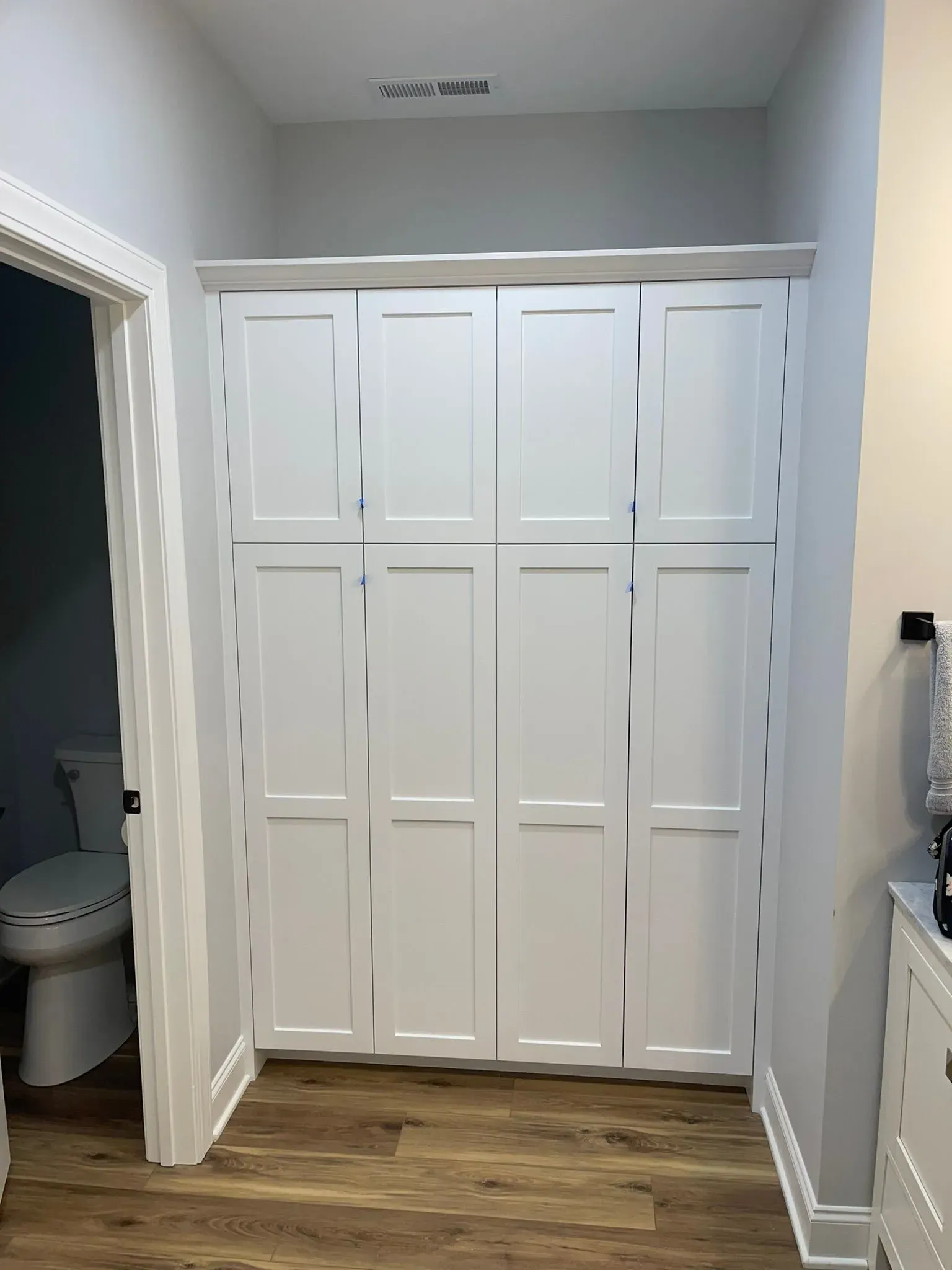 White double closet doors in a small hallway with light gray walls and wood flooring.