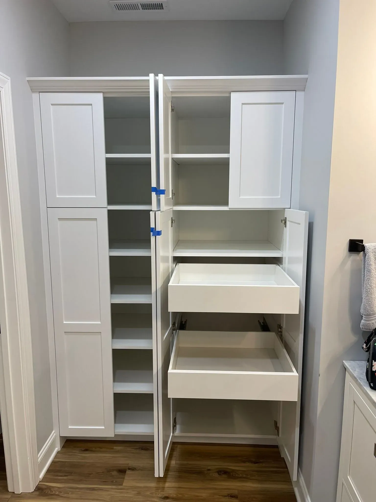 Open closet with white shelving and drawers in a small gray room, cabinets and pull-out shelves visible.