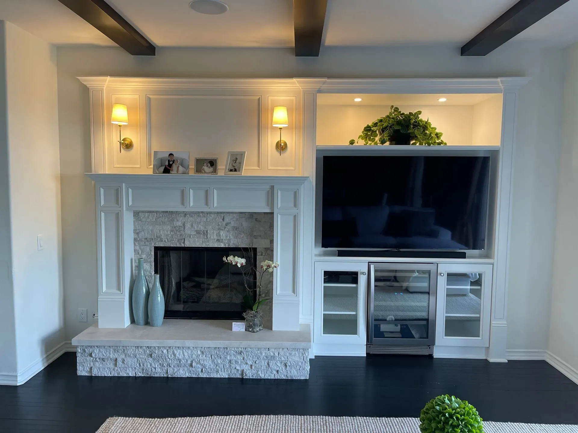 Living room with white fireplace mantel, wall-mounted TV, built-in shelves, and dark wood ceiling beams