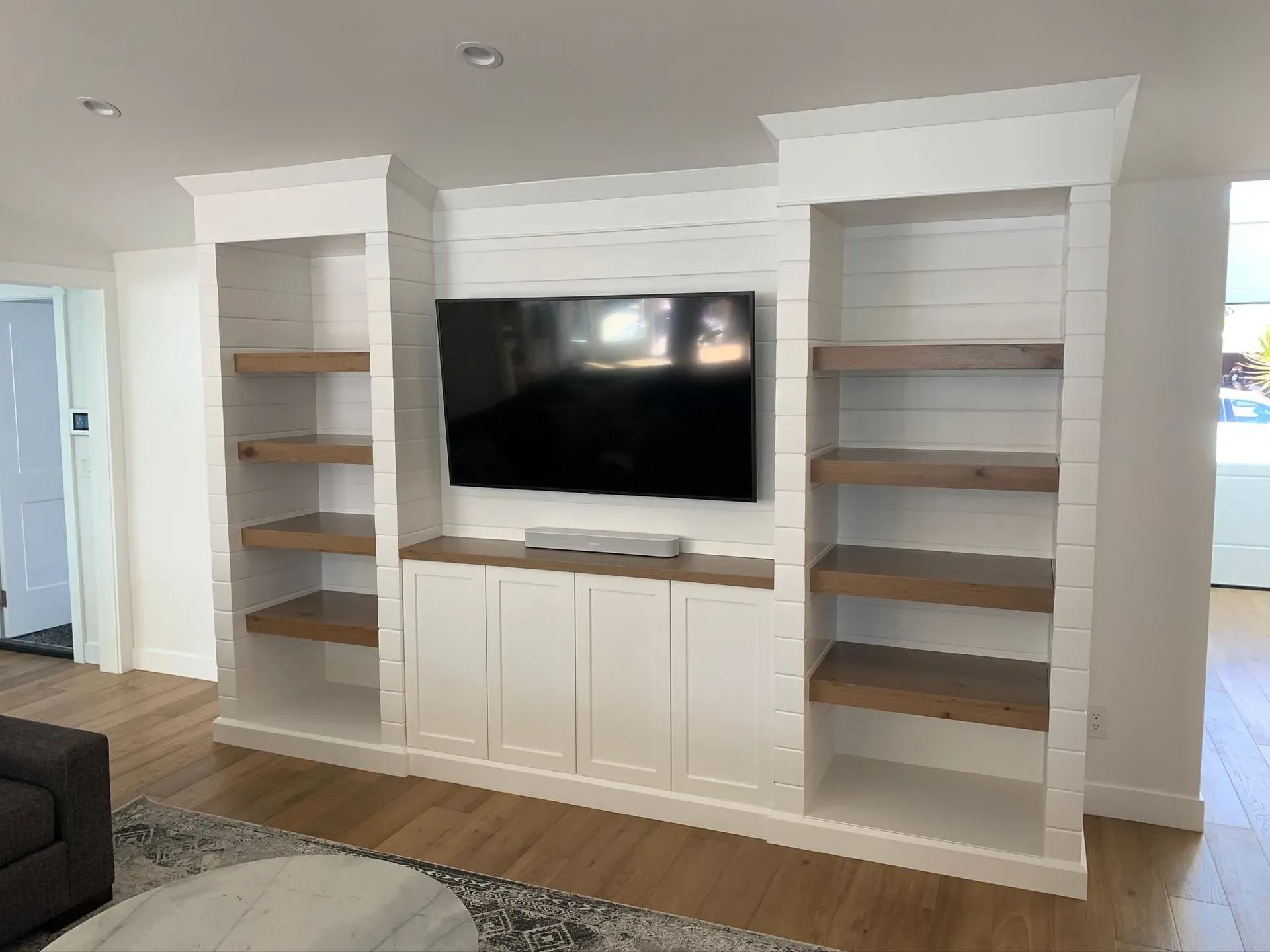 Built-in white entertainment center with TV and empty shelves in a bright living room