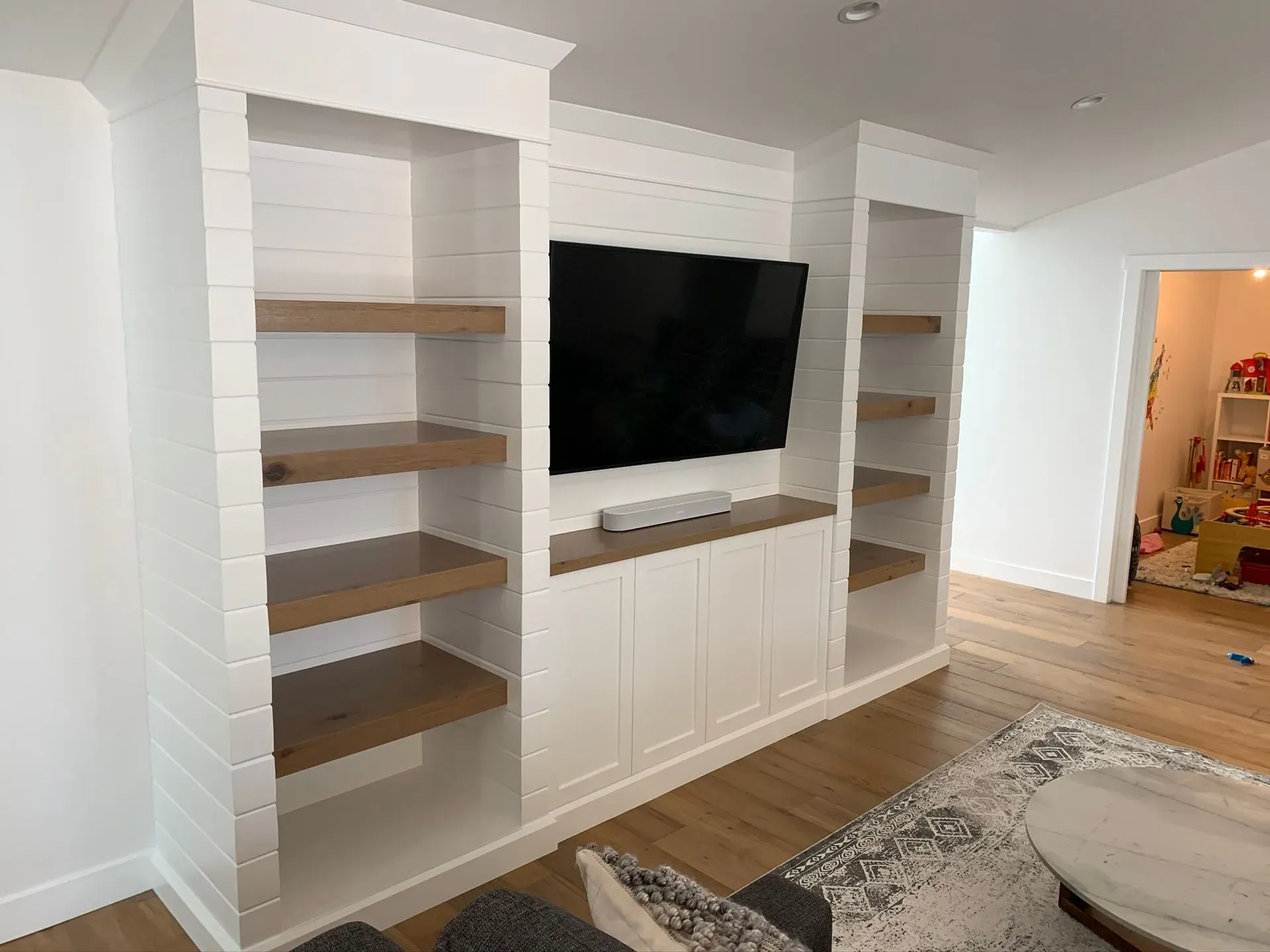 Built-in white shelving and cabinets with a wall-mounted TV in a bright living room