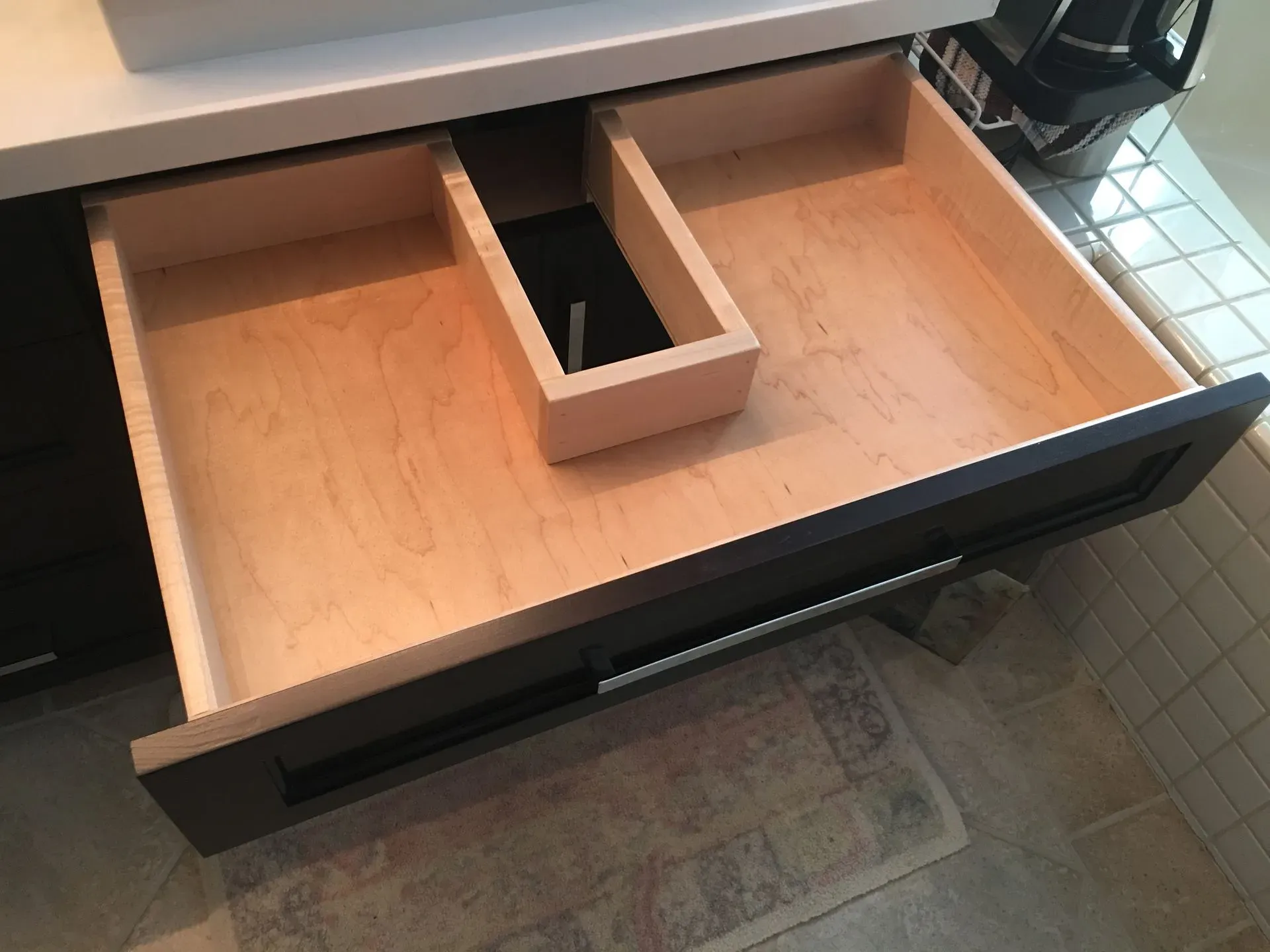 Open drawer with a wooden tray organizer and a black rectangular compartment inside.