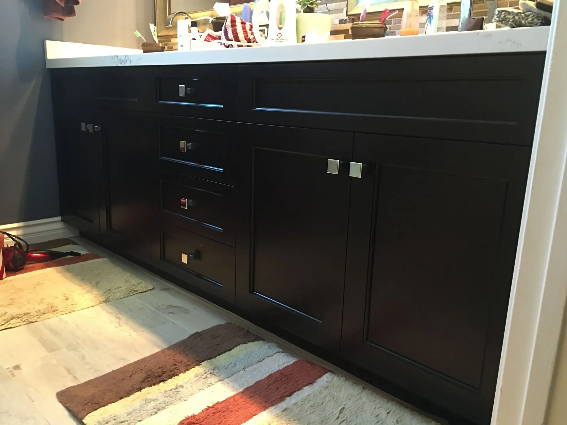 Black kitchen lower cabinets and drawers beneath a countertop, with a striped rug on the floor.