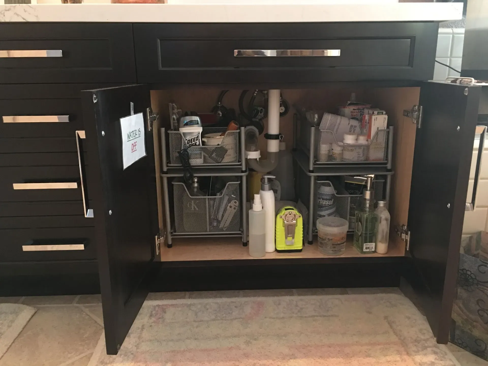 Open black kitchen cabinet with organized cleaning supplies and storage bins inside.