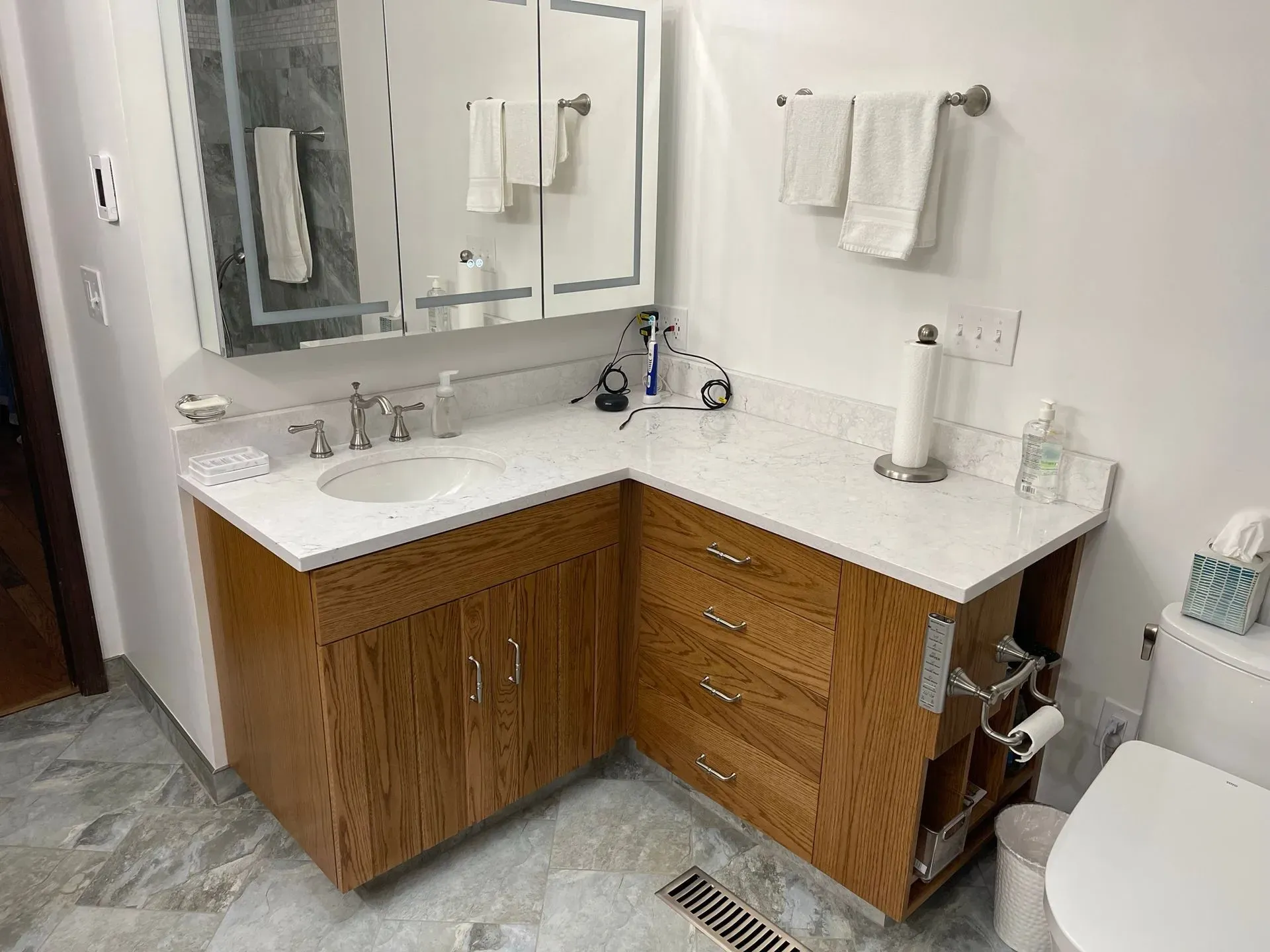 Modern bathroom vanity with double mirrors, white countertops, wood cabinets, and a toilet on the right