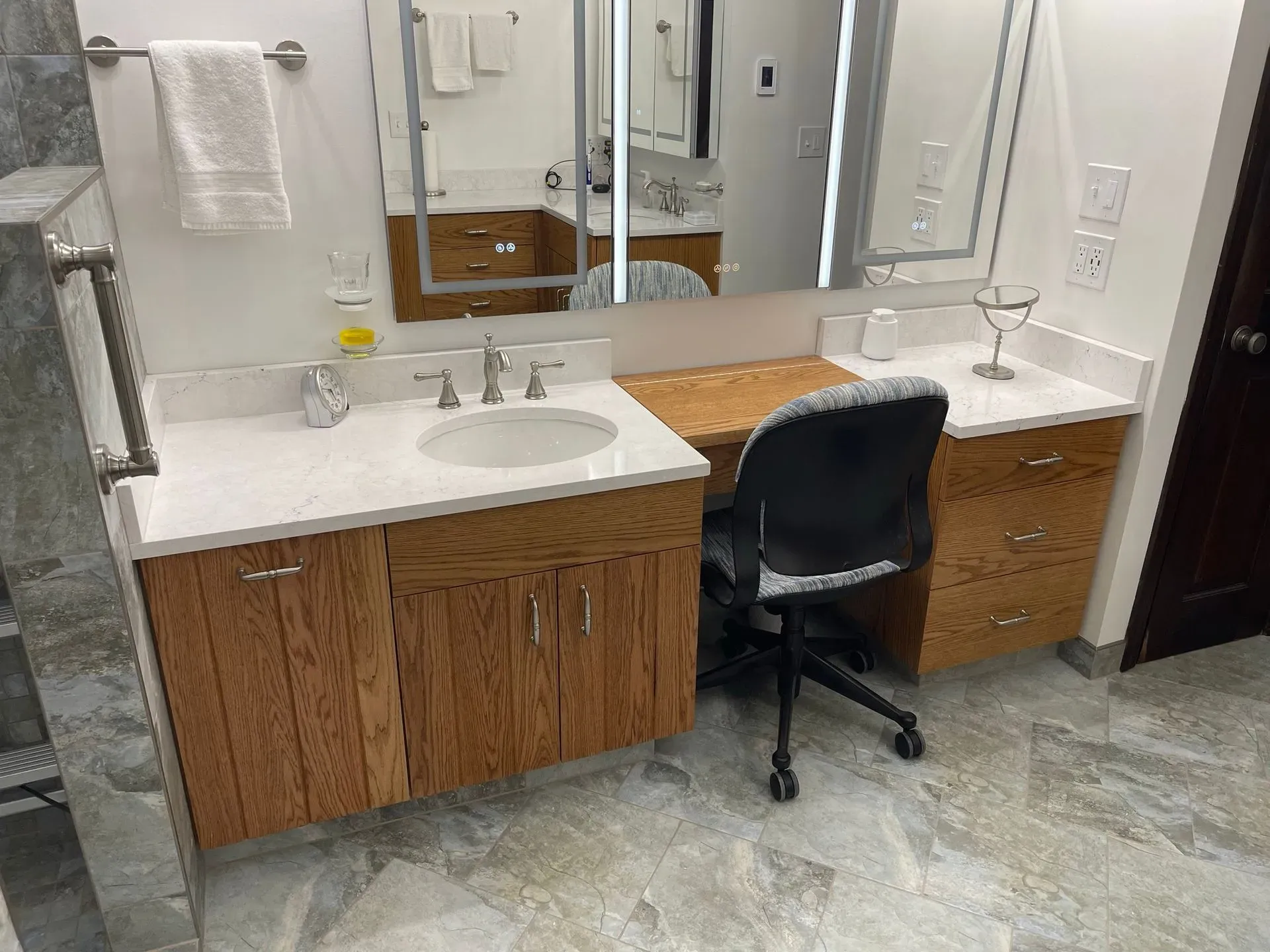 Bathroom vanity with two sinks, mirror, and black chair in front of a wood cabinet counter.