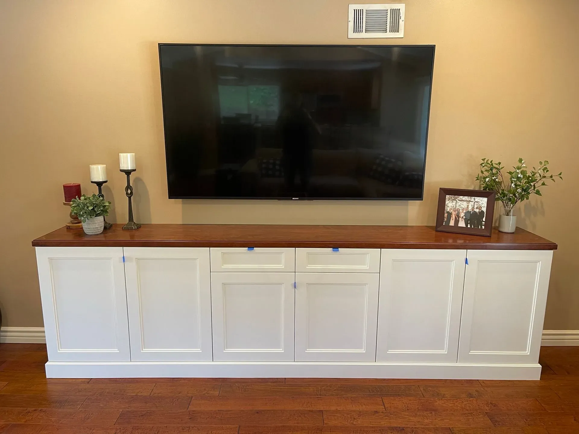 White media console with TV, candles, framed photo, and plant in a living room