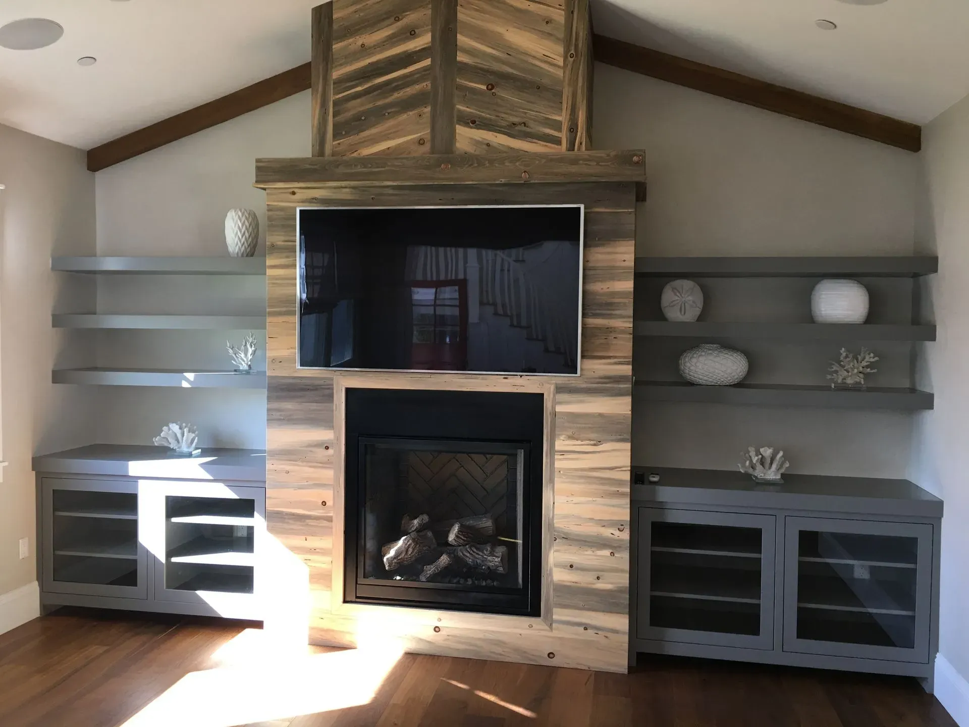 Modern living room with a stone fireplace, built-in shelves, and gray cabinets beside it
