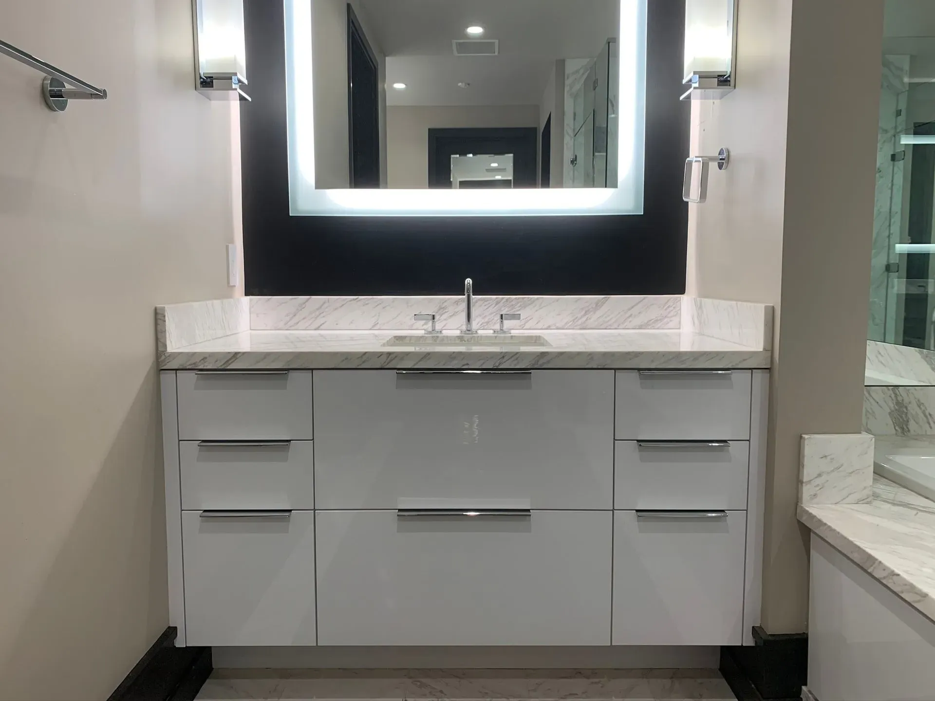 Modern bathroom vanity with white cabinets, marble countertop, mirror, and wall sconces