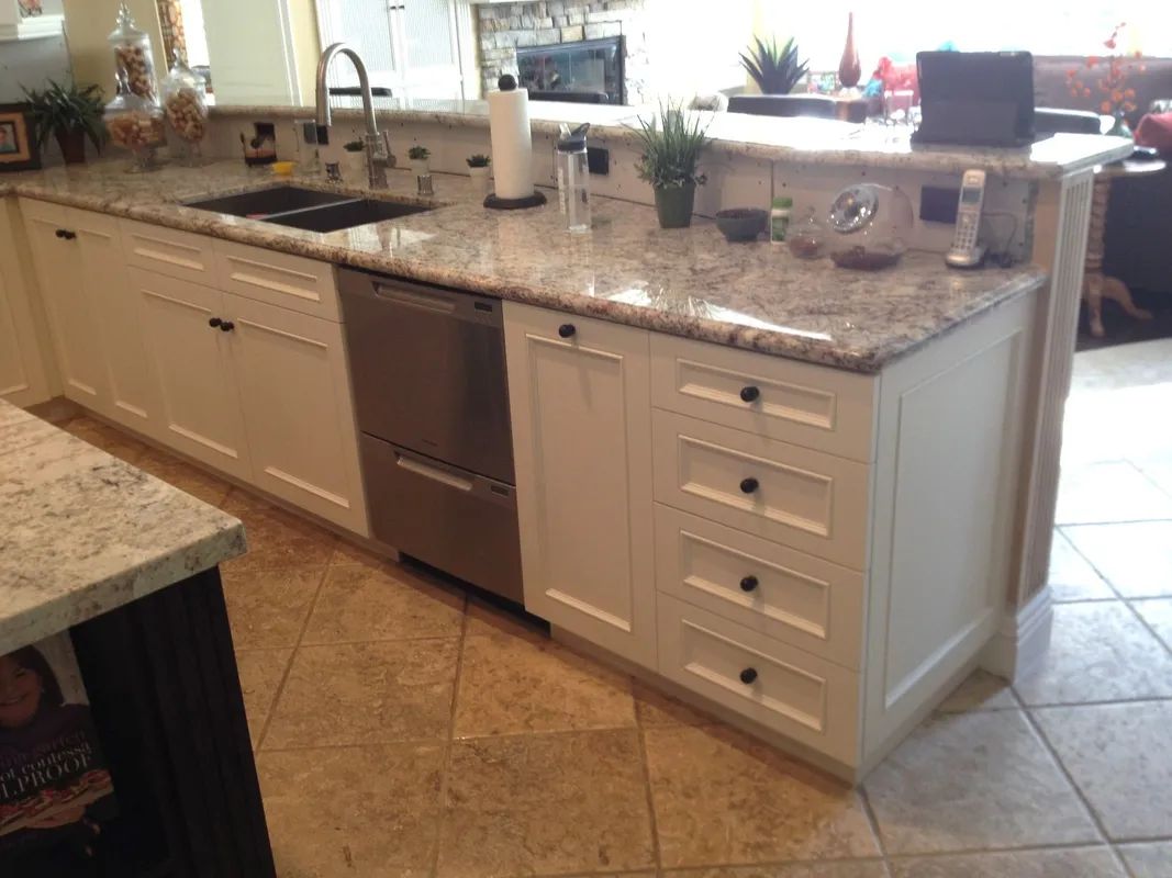 Modern kitchen with granite countertops, white cabinets, stainless dishwasher, and tiled floor.
