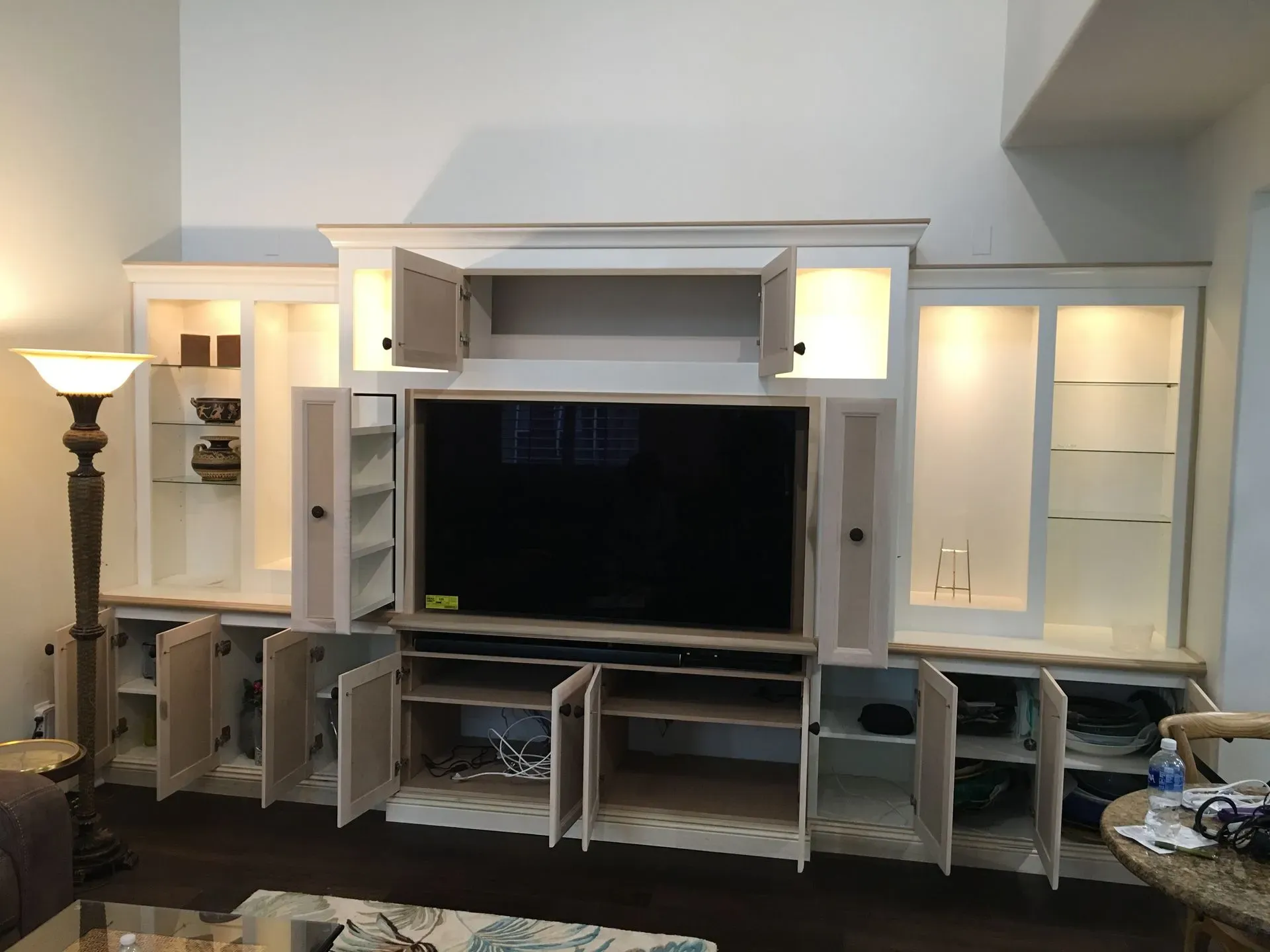 Living room wall unit with TV, built-in shelves, and cabinet doors, with several doors open and a floor lamp nearby