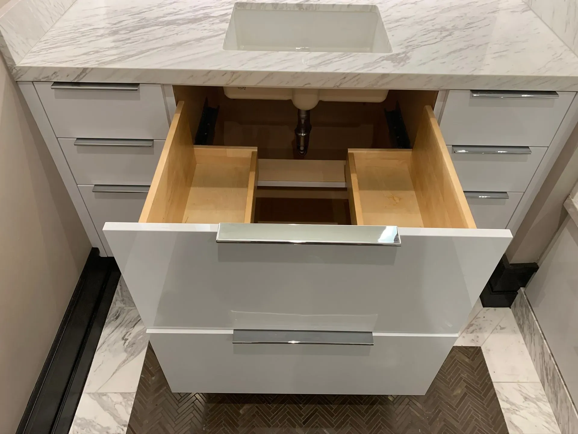 Open bathroom vanity drawer with light wood organizers and a white sink above.