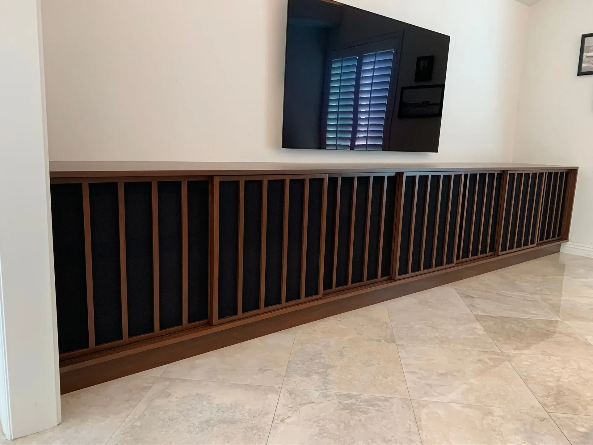 Long wooden cabinet with black panels beneath a wall-mounted TV in a tiled room