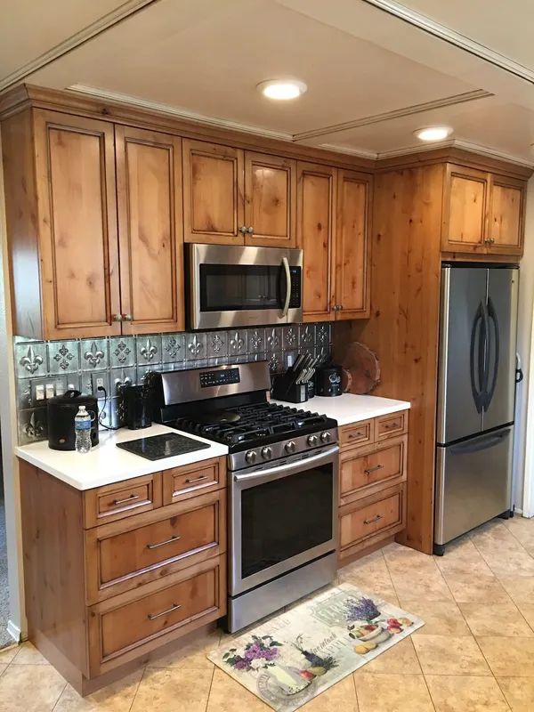 Wooden kitchen with stainless steel stove and refrigerator, tile backsplash, and patterned floor rug.