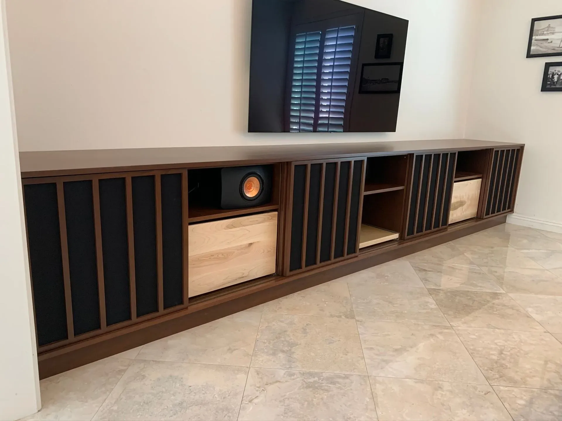 Built-in wooden media cabinet beneath a wall-mounted TV in a bright room with tiled floor