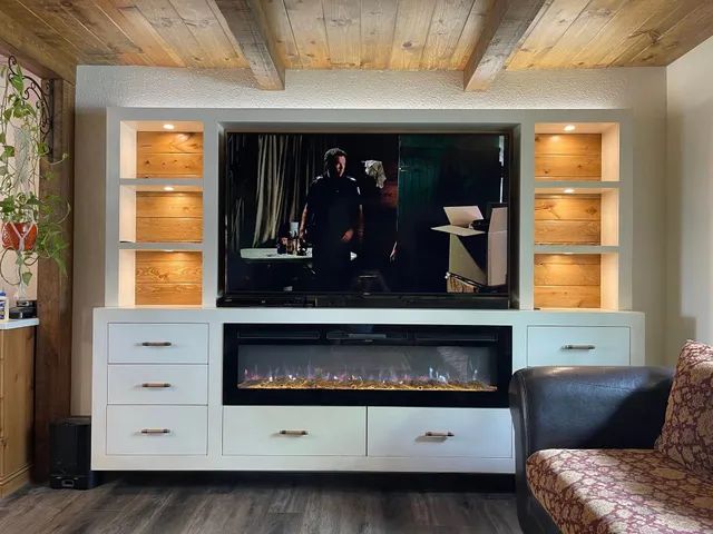 Living room wall with built-in fireplace, TV, white cabinets, and warm wood ceiling accents