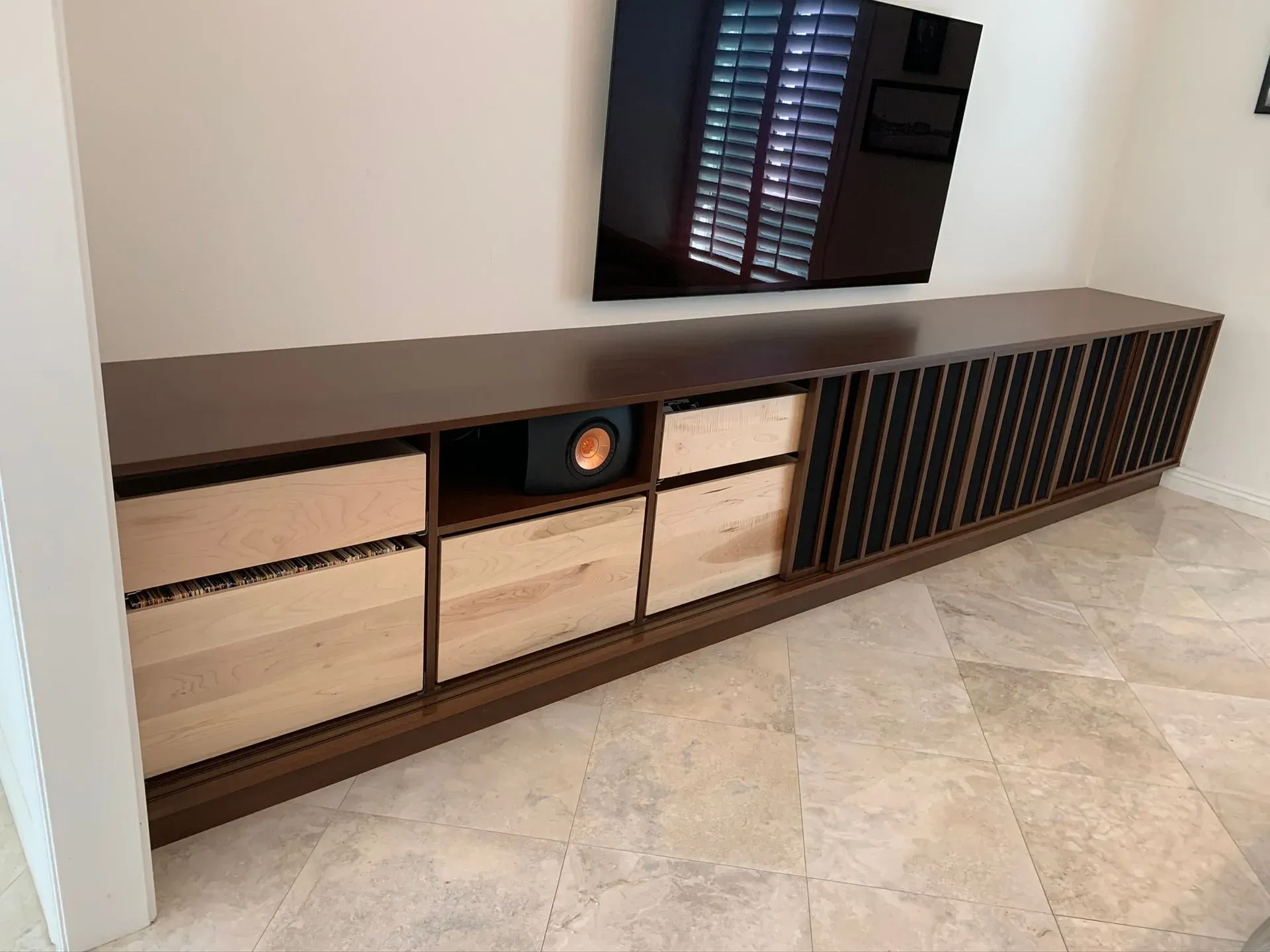 Modern dark wood TV console with drawers and slatted cabinet in a bright room, with a TV on top