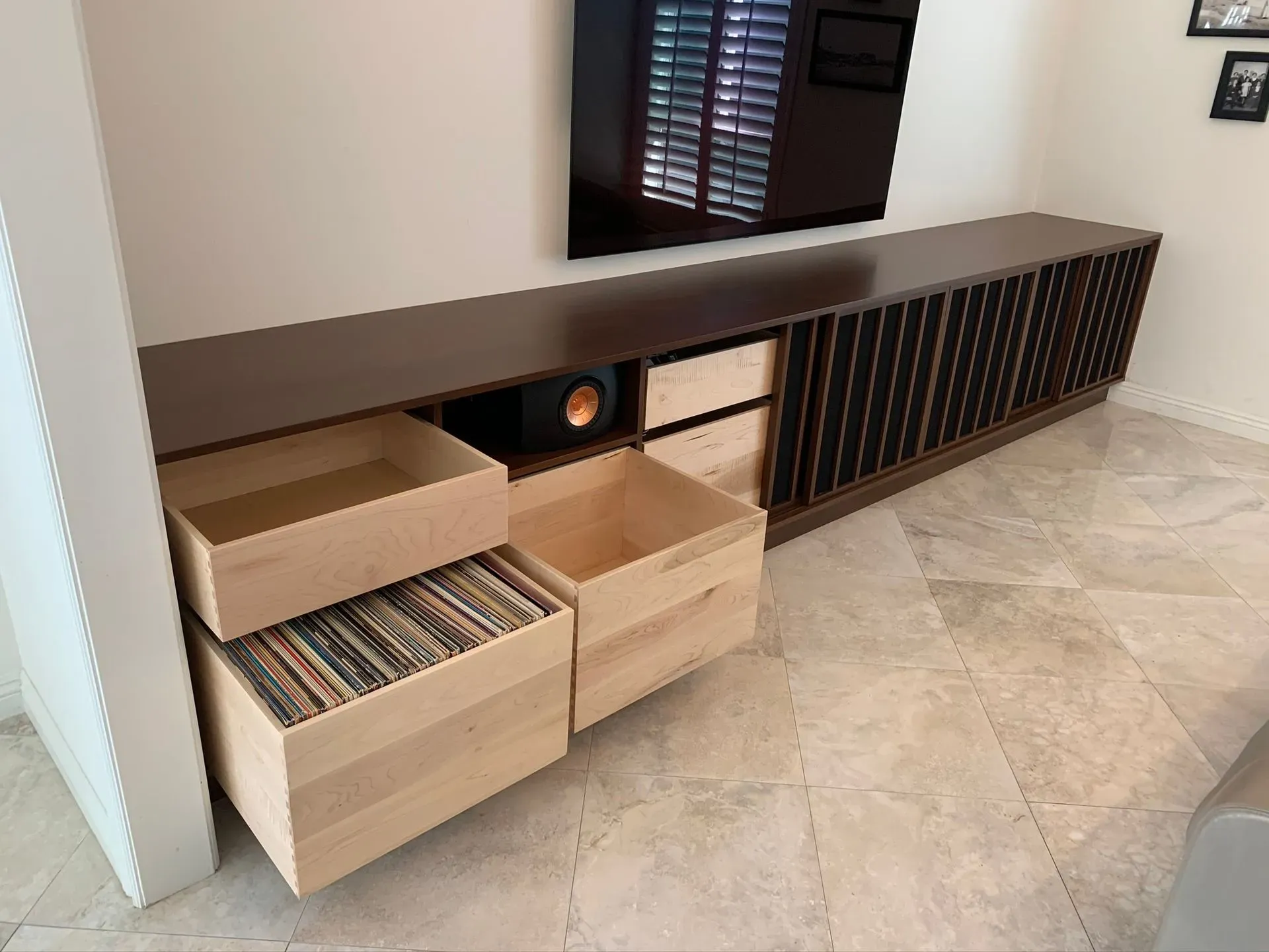 Modern TV console with open drawers, vinyl records, and a wall-mounted TV in a tiled living room
