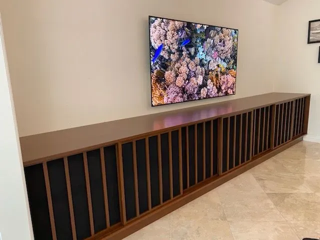 Wall-mounted TV above a long wooden console with black panels in a modern hallway.
