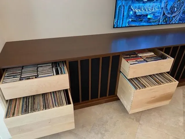 Wooden cabinet with open vinyl record storage bins in a room, brown top and beige drawers.