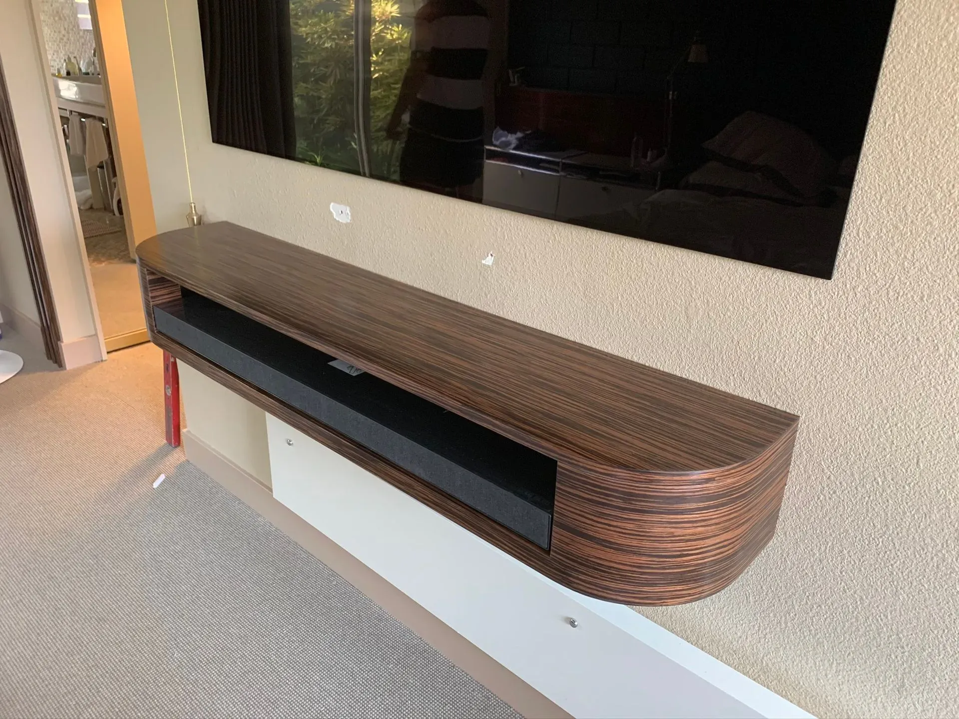 Wall-mounted woven wood TV console with a black shelf beneath a large TV in a modern room