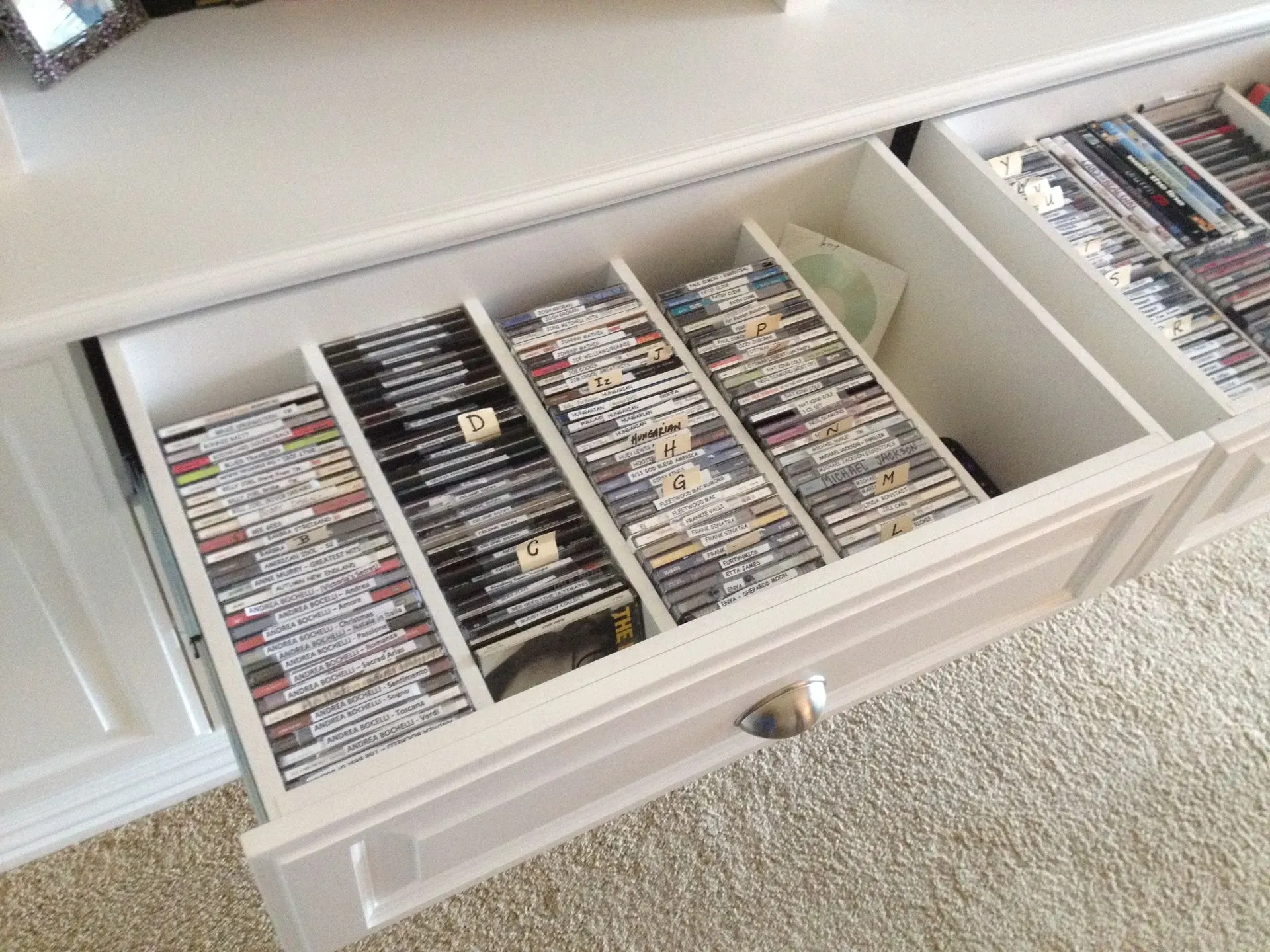 Open drawer filled with rows of DVDs or CDs in white cabinet