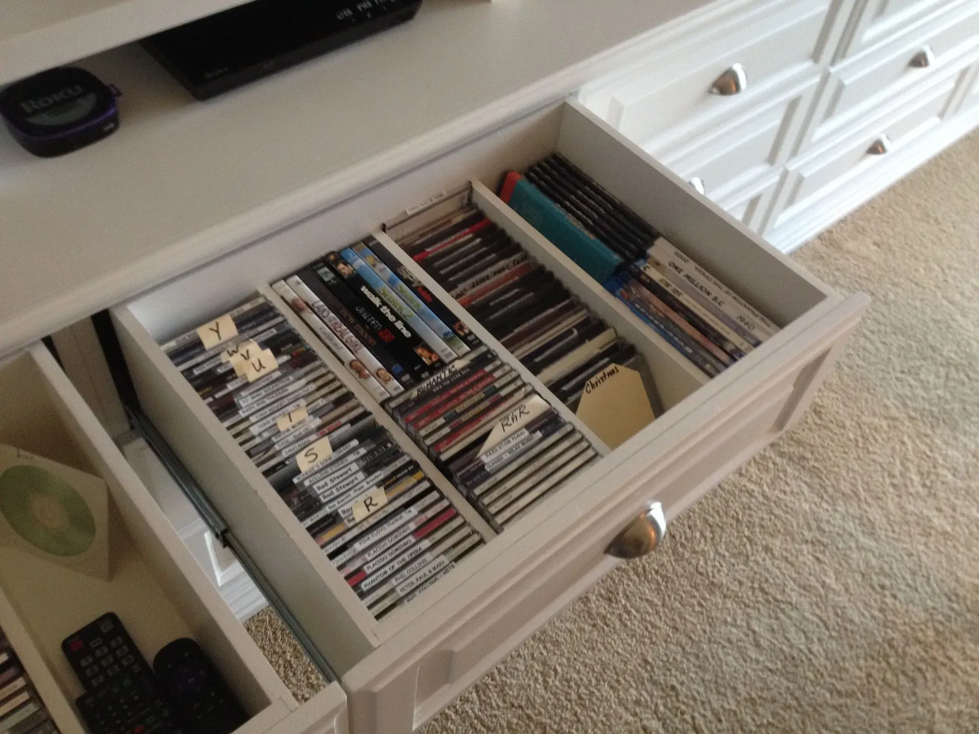 Open drawer filled with rows of DVDs and video games next to a TV stand