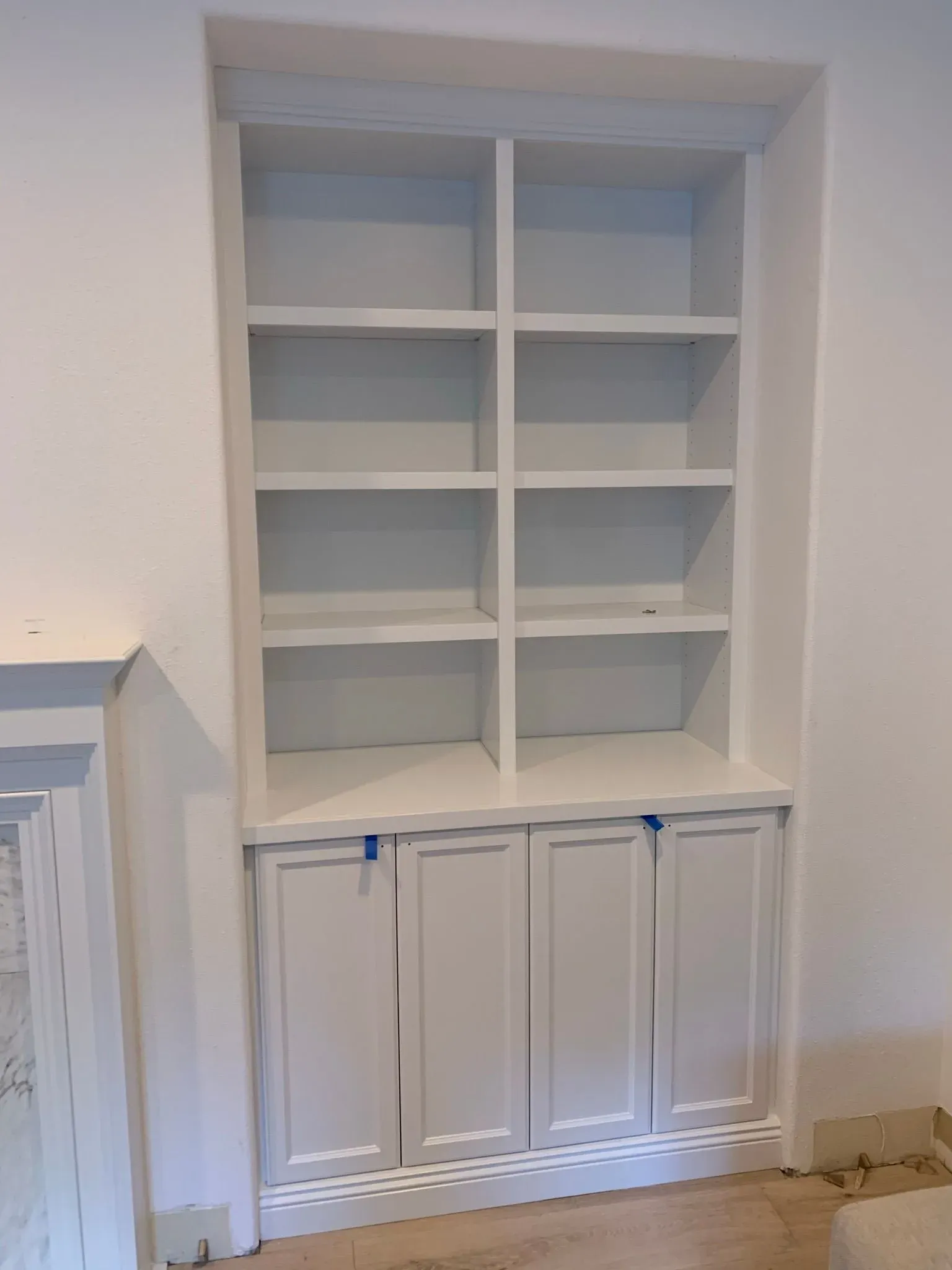 White built-in shelving unit with cubbies above cabinet doors in a room under renovation