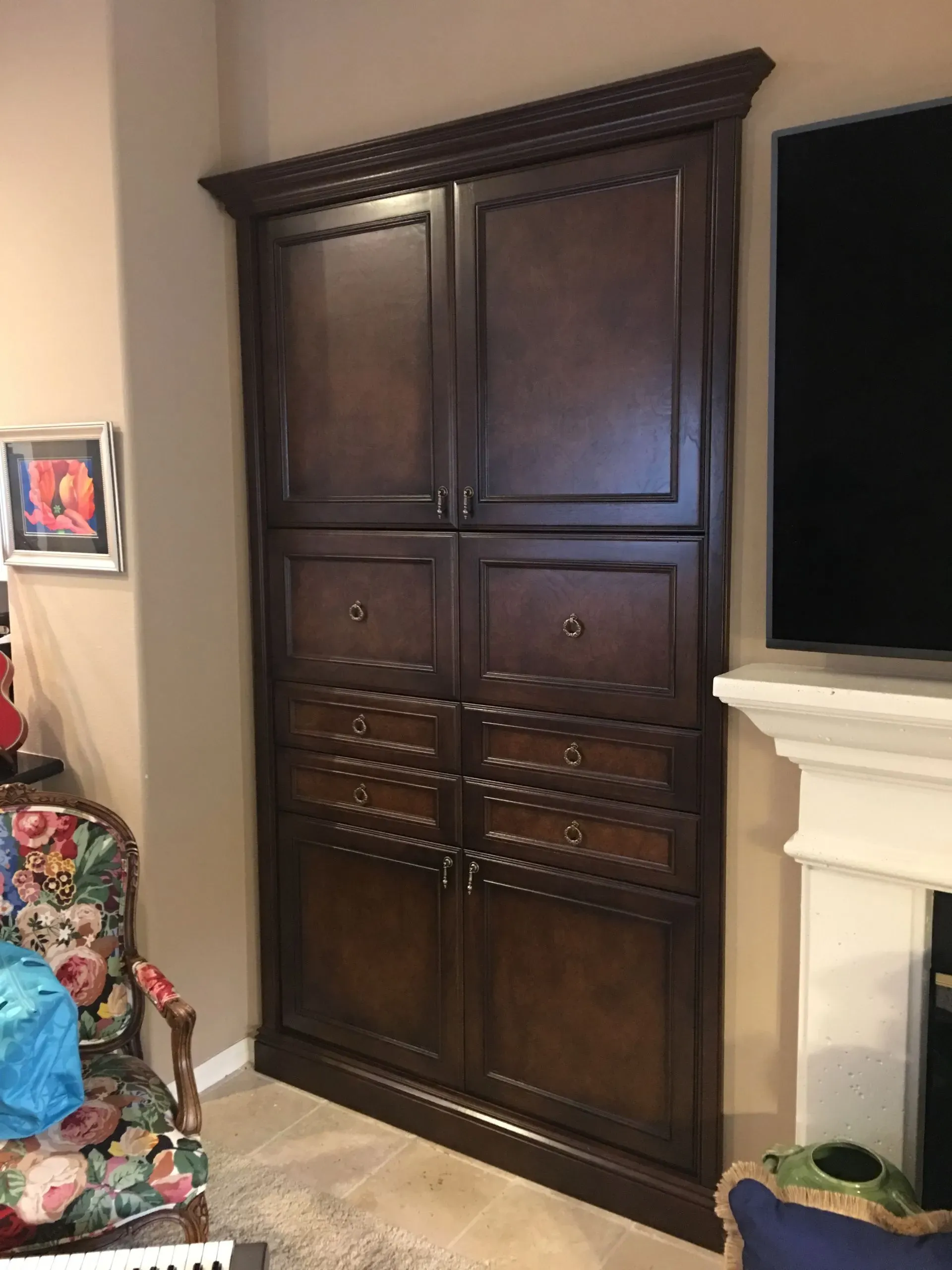 Tall dark wood cabinet with paneled doors and drawers in a carpeted living room beside a fireplace.