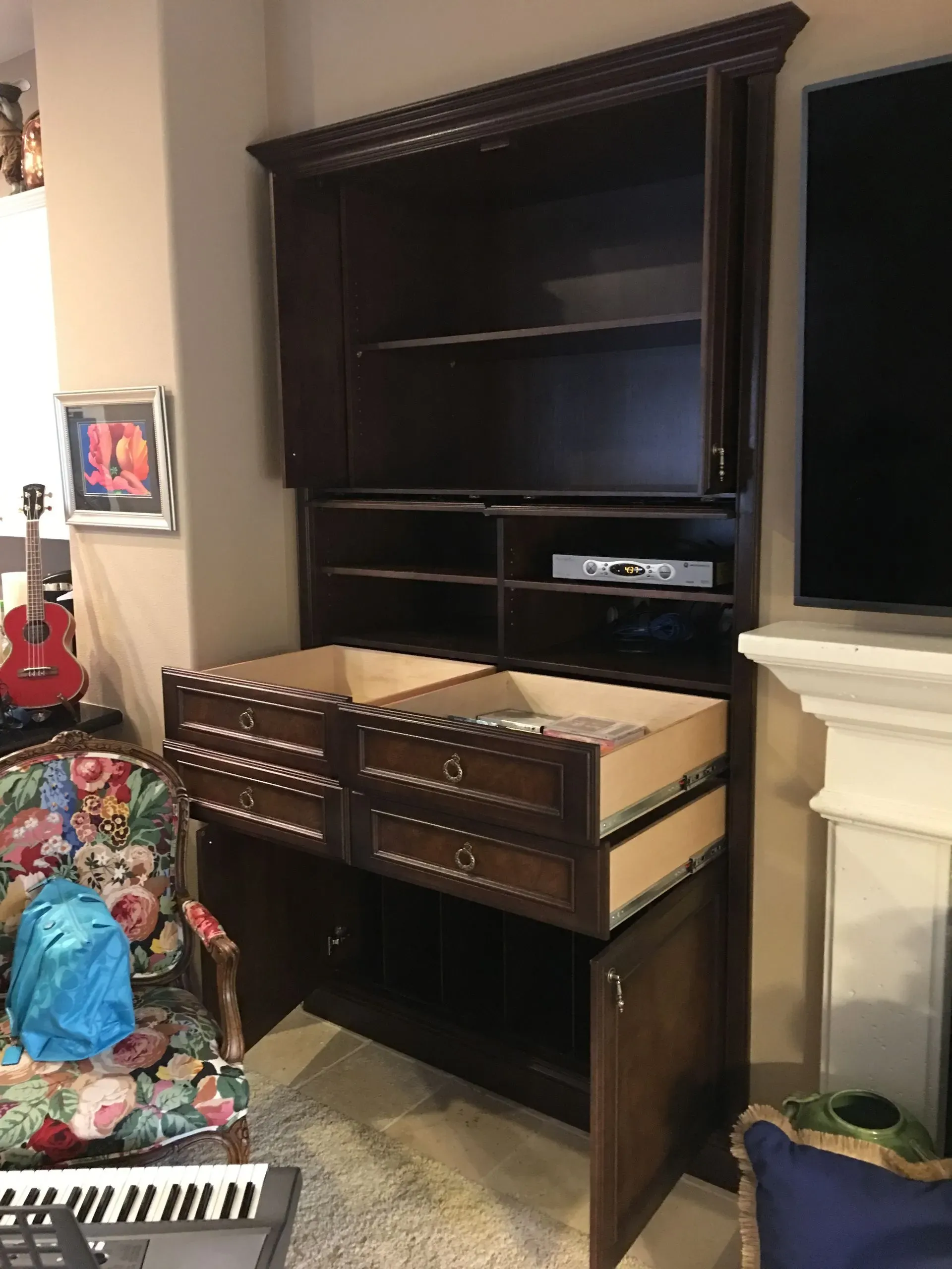 Dark wood cabinet with drawers and shelves in a living room beside a fireplace and colorful couch