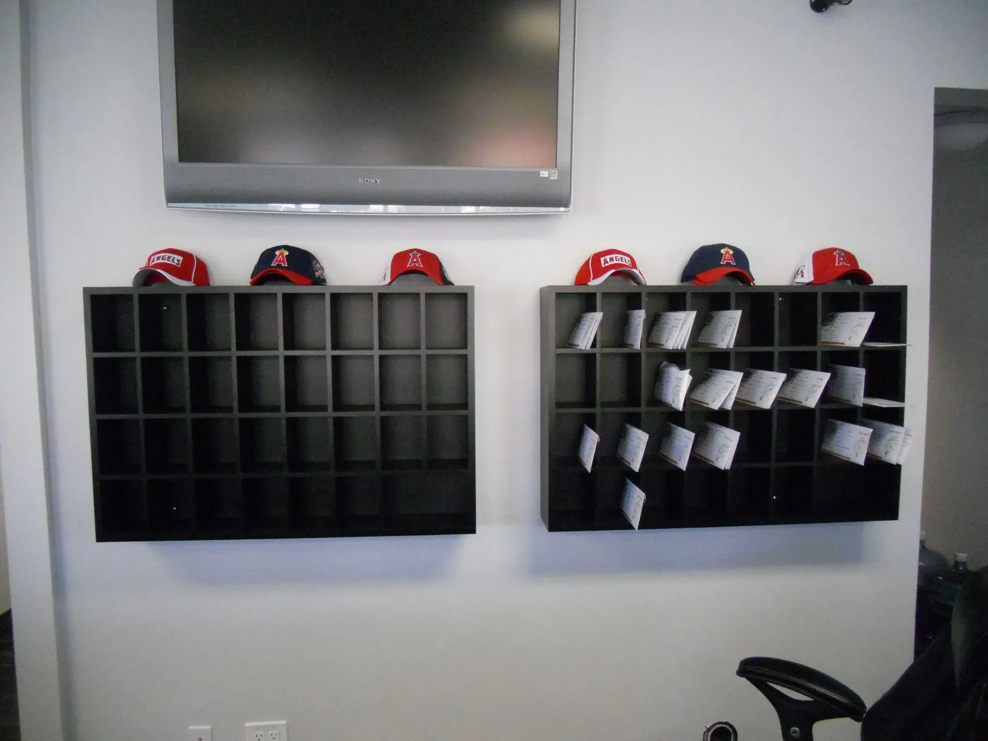 Wall-mounted black cubbies under a TV, with red-and-black caps on top and papers in the right organizer.
