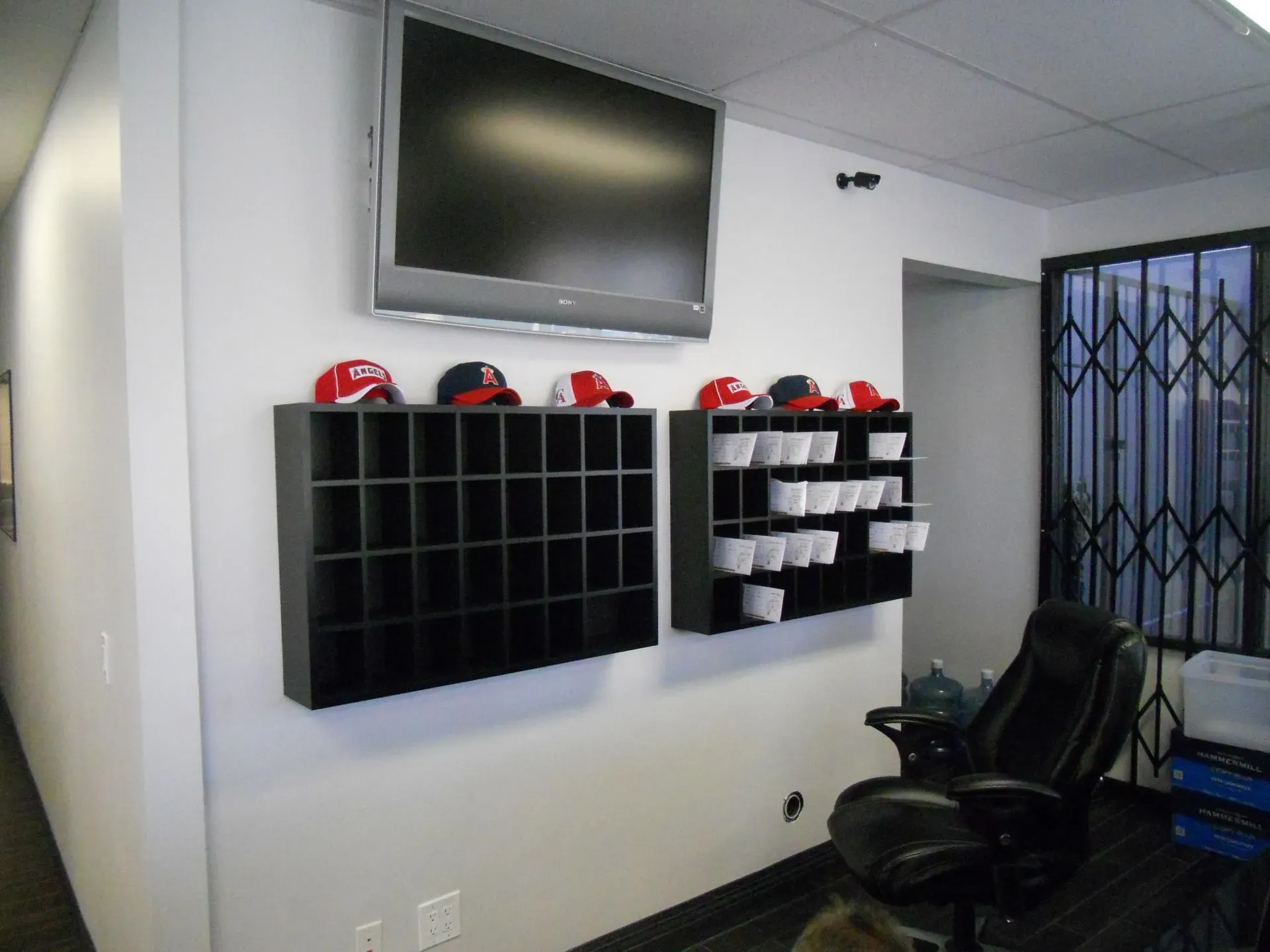 Wall-mounted TV above black helmet cubbies in a small office or locker room