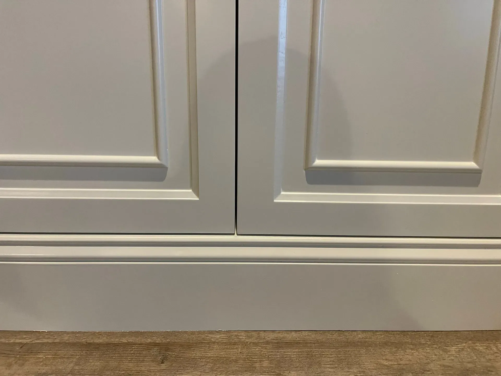 White cabinet doors with panels and a silver baseboard or drawer trim.