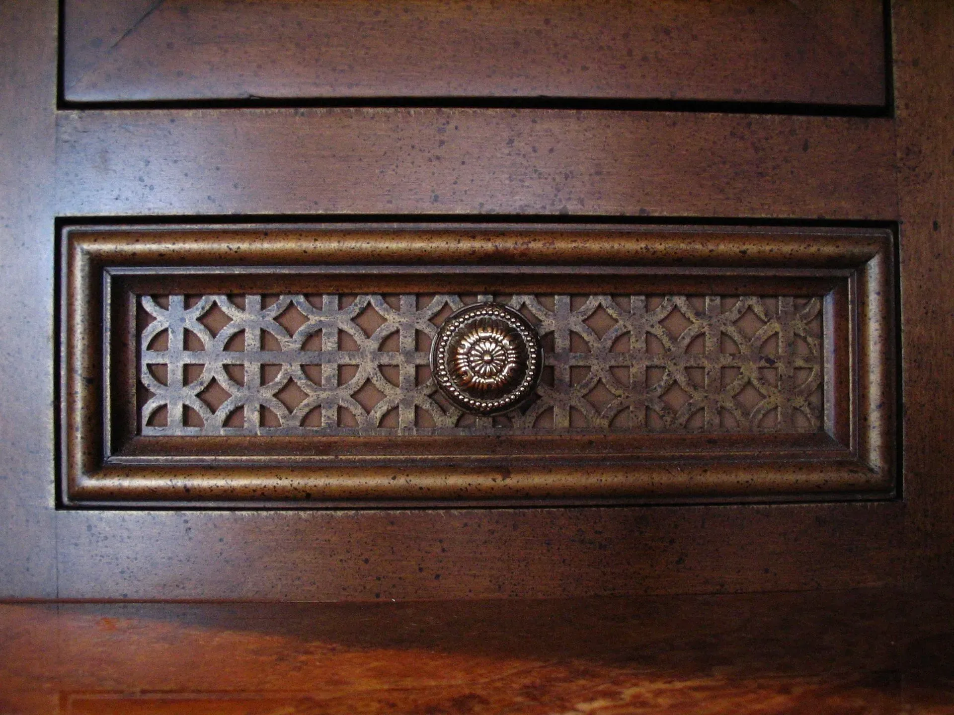 Ornate wooden door panel with a decorative metal grille and central knob in brown tones