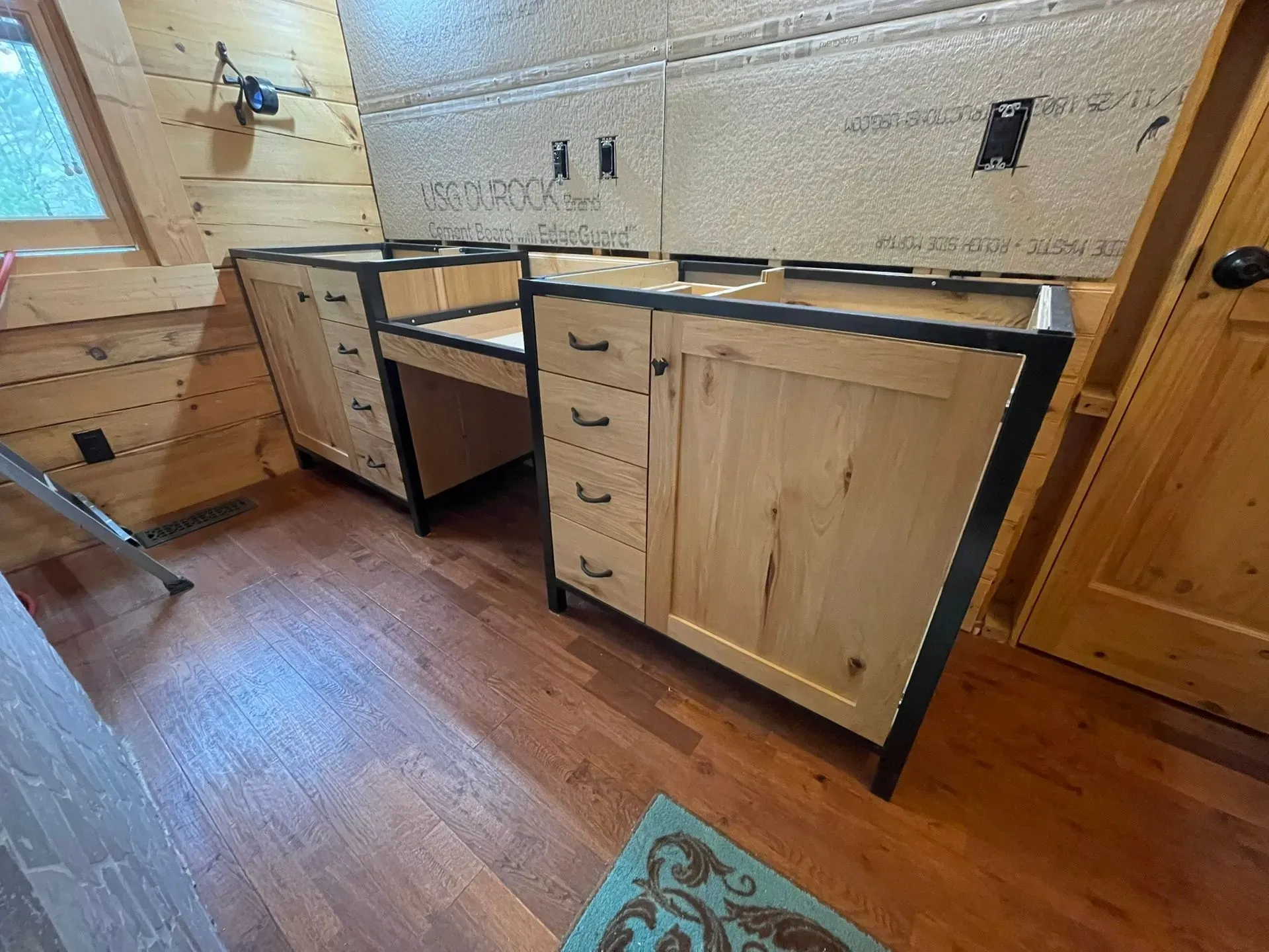 Wooden kitchen cabinets with black countertops in a small rustic room, seen from a low angle.