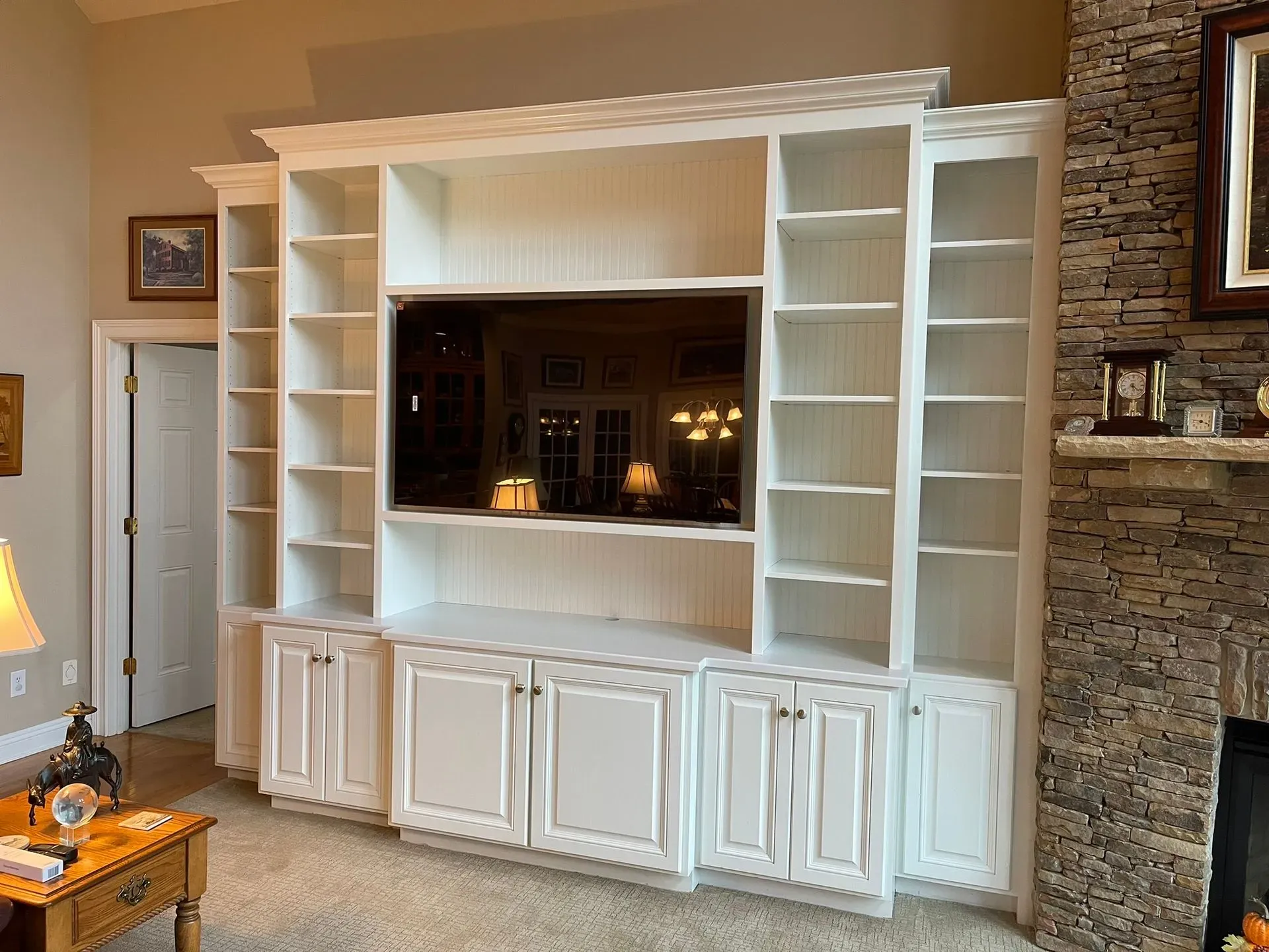 Built-in white shelving and cabinets framing a living room fireplace with a stone surround