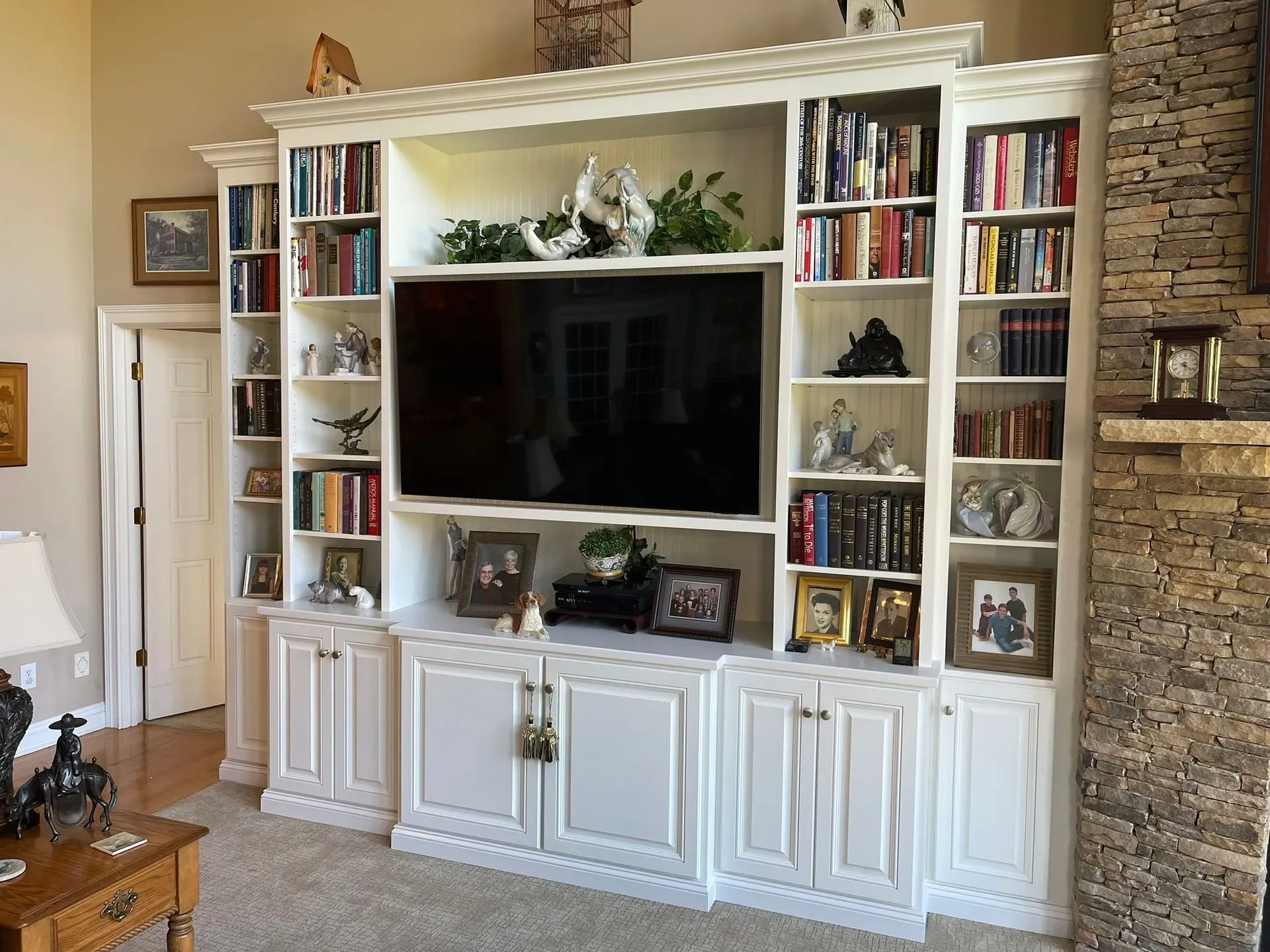 Built-in white entertainment center with TV, books, and decor beside a stone fireplace in a living room