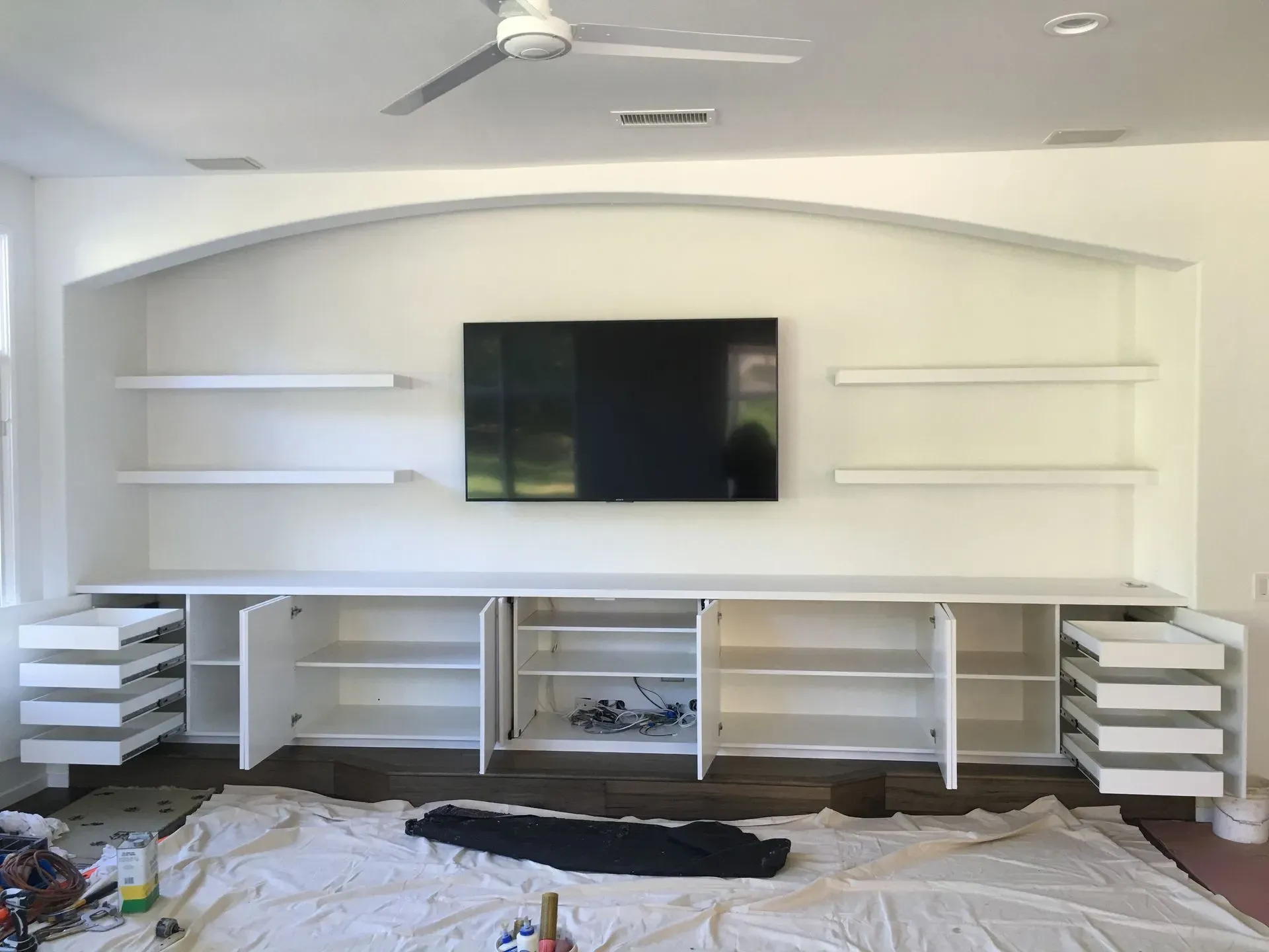 Living room media wall under renovation with built-in shelves, cabinets, and a mounted TV.