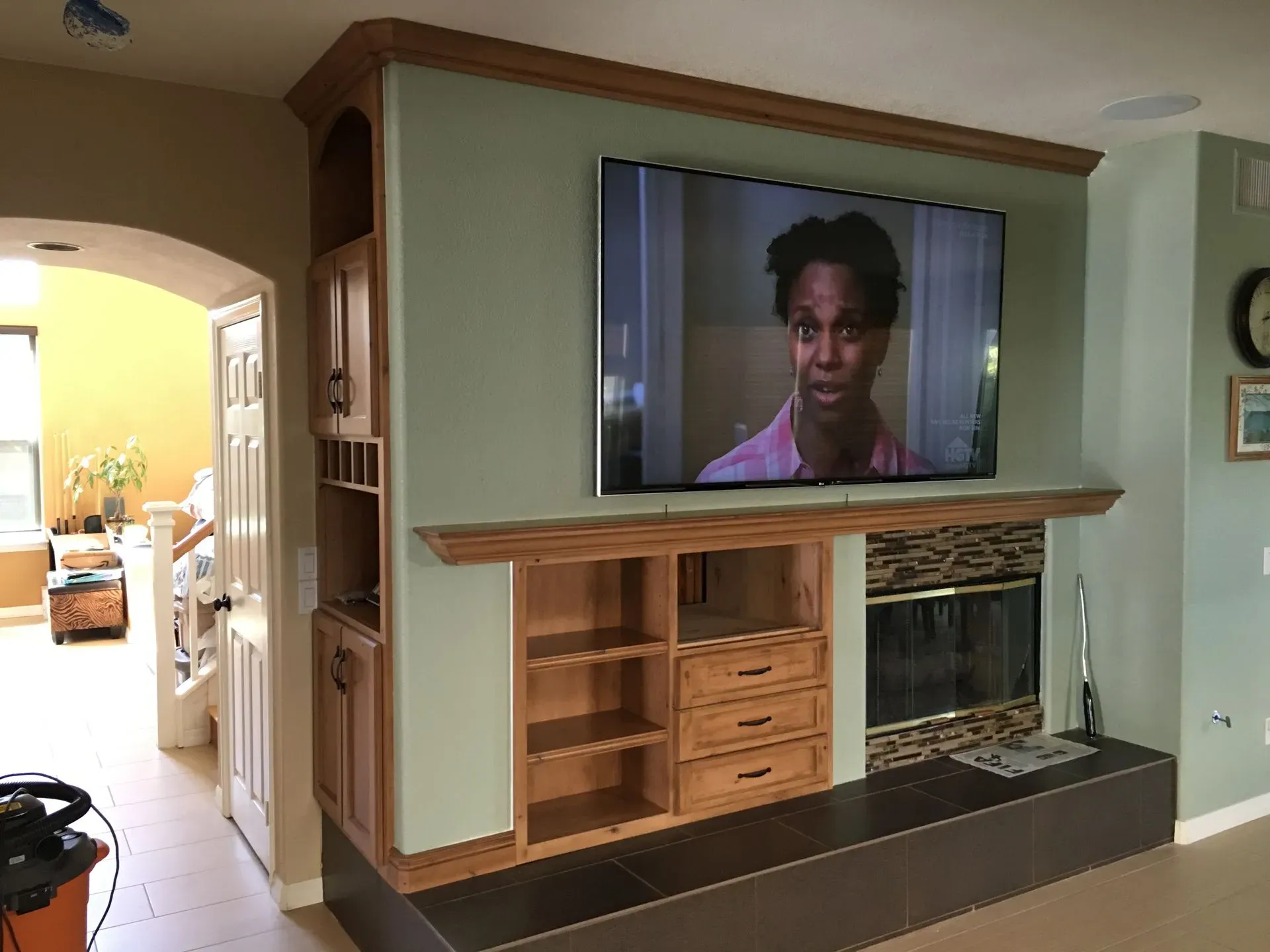 Living room with a large TV above an unfinished wooden fireplace surround and built-in shelving