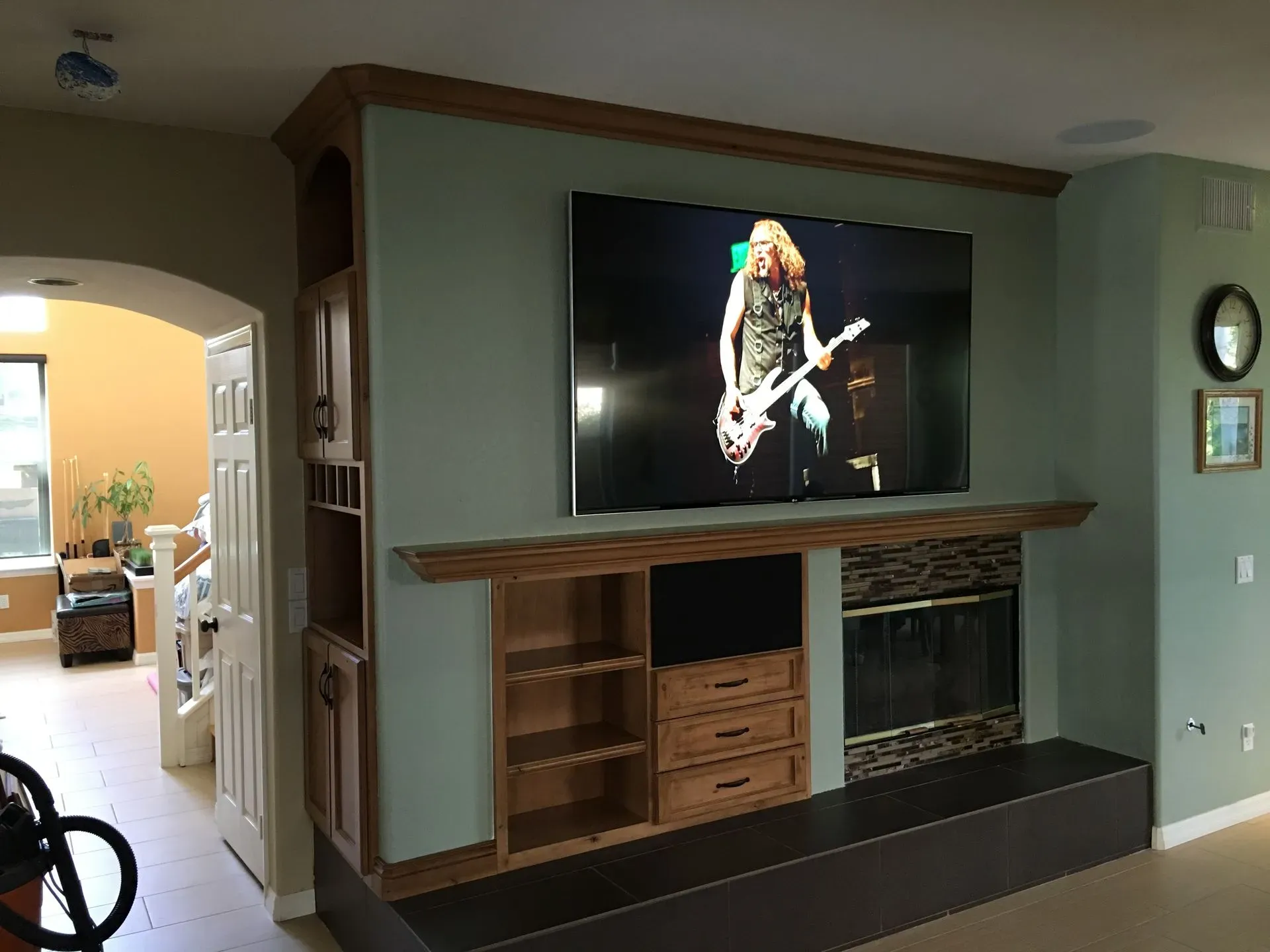 Living room wall-mounted TV above a wooden fireplace mantel, with a music performance on screen
