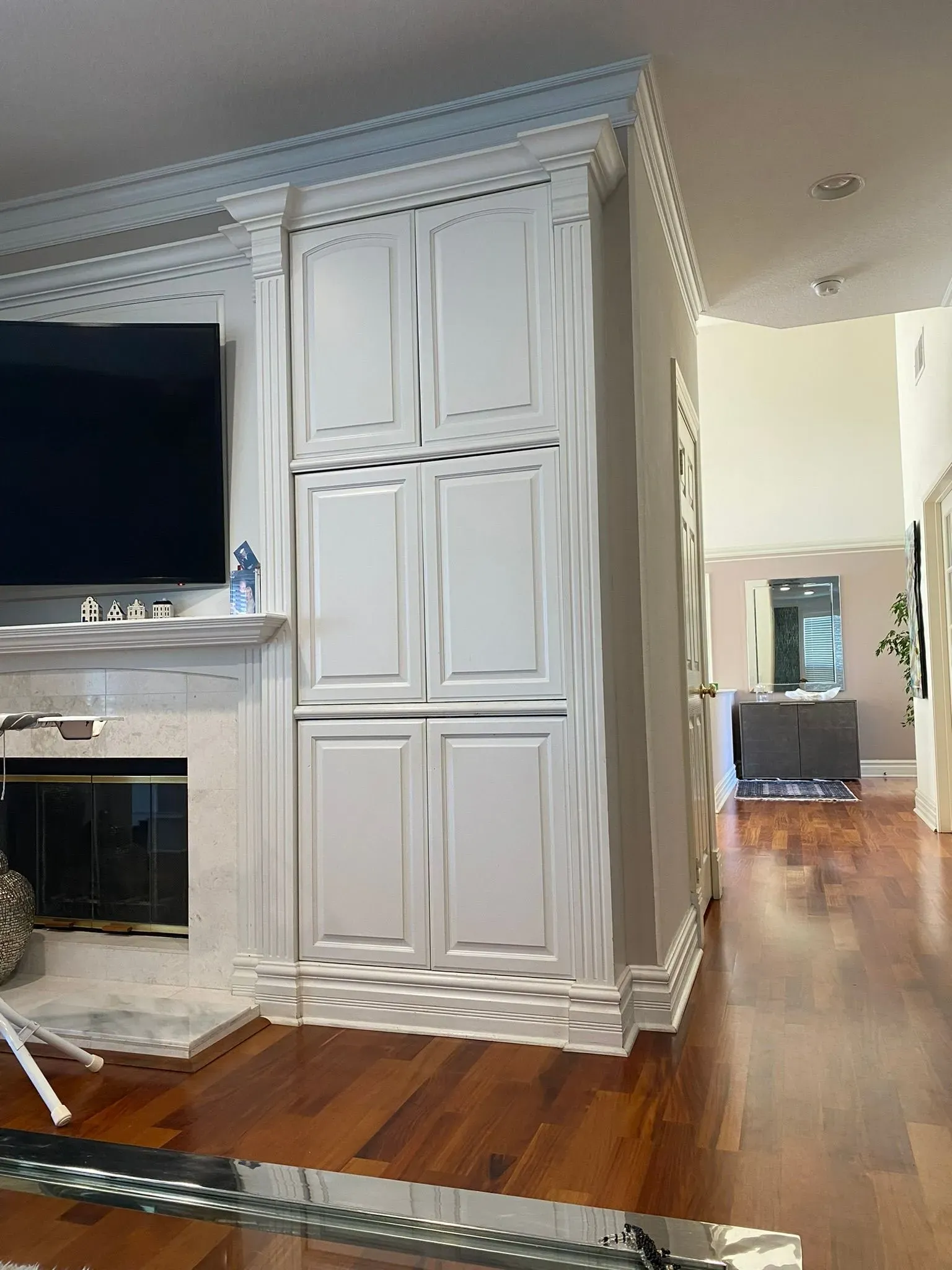 Living room with white built-in cabinets, fireplace, and hardwood floors leading to a hallway