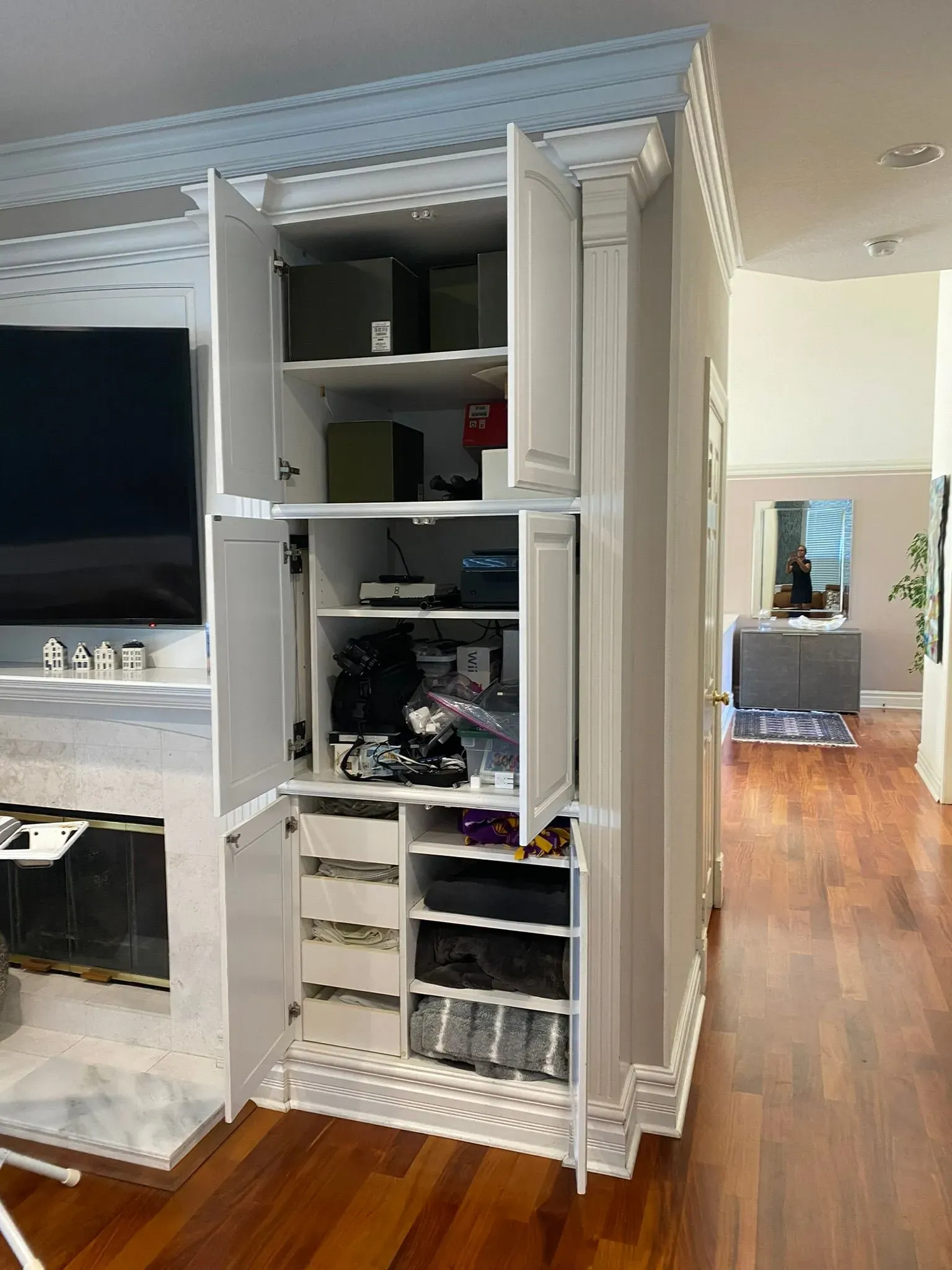 White built-in shelving with cabinets and electronics in a bright living room; wood floor and doorway in background