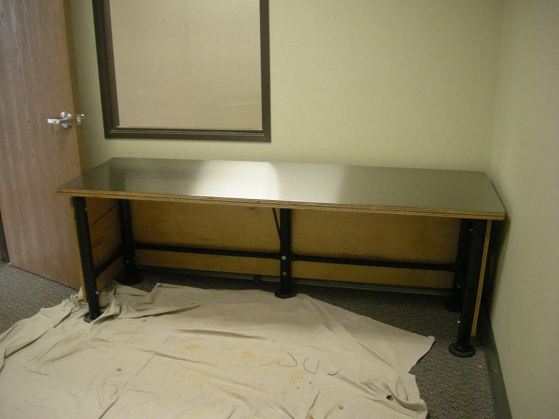 Long black table against a wall in an unfinished room with drop cloths on the floor
