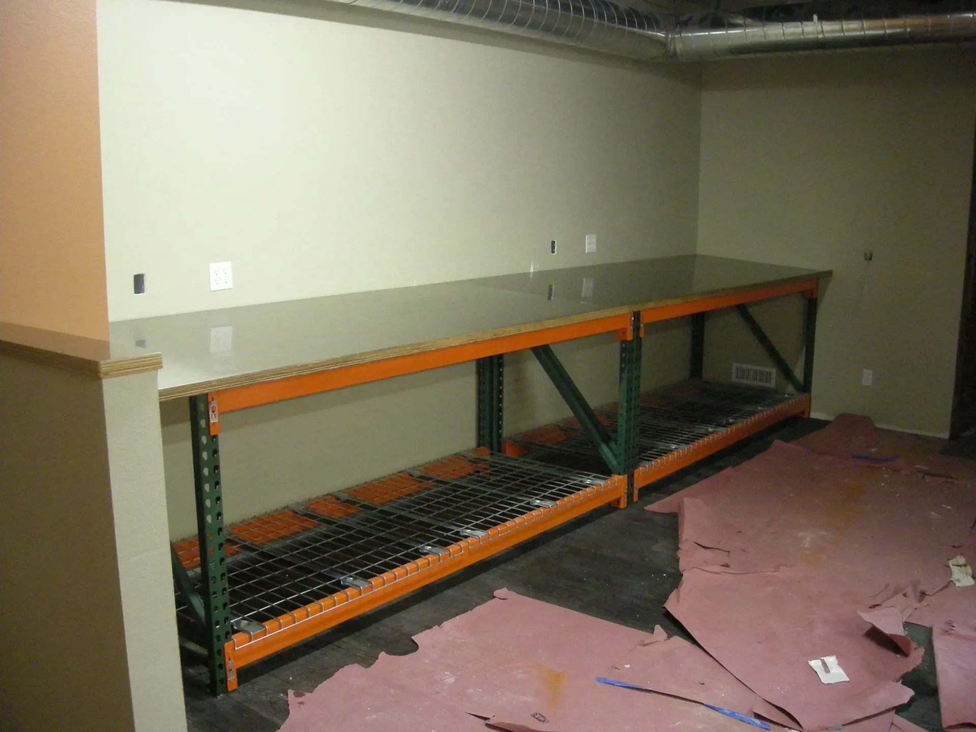 Damaged room with a long orange-and-green metal shelf and torn pink carpet panels on the floor.